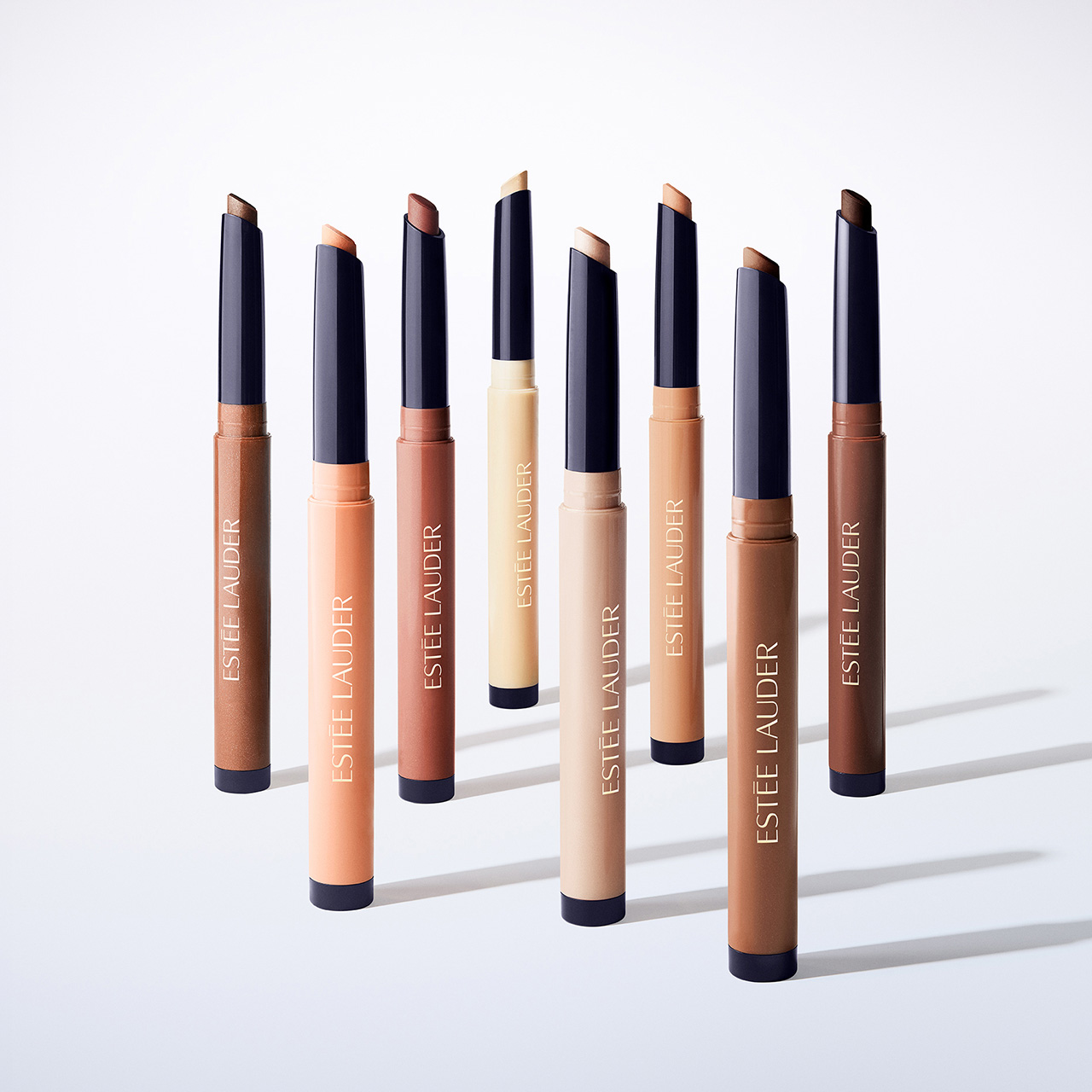 Eight Estée Lauder eyeshadow stick products in various nude and bronze shades arranged in rows