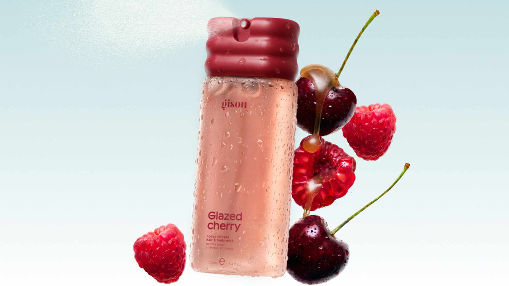 Pink hair and body mist bottle with red cherry and raspberry fruits arranged beside it against a light blue background