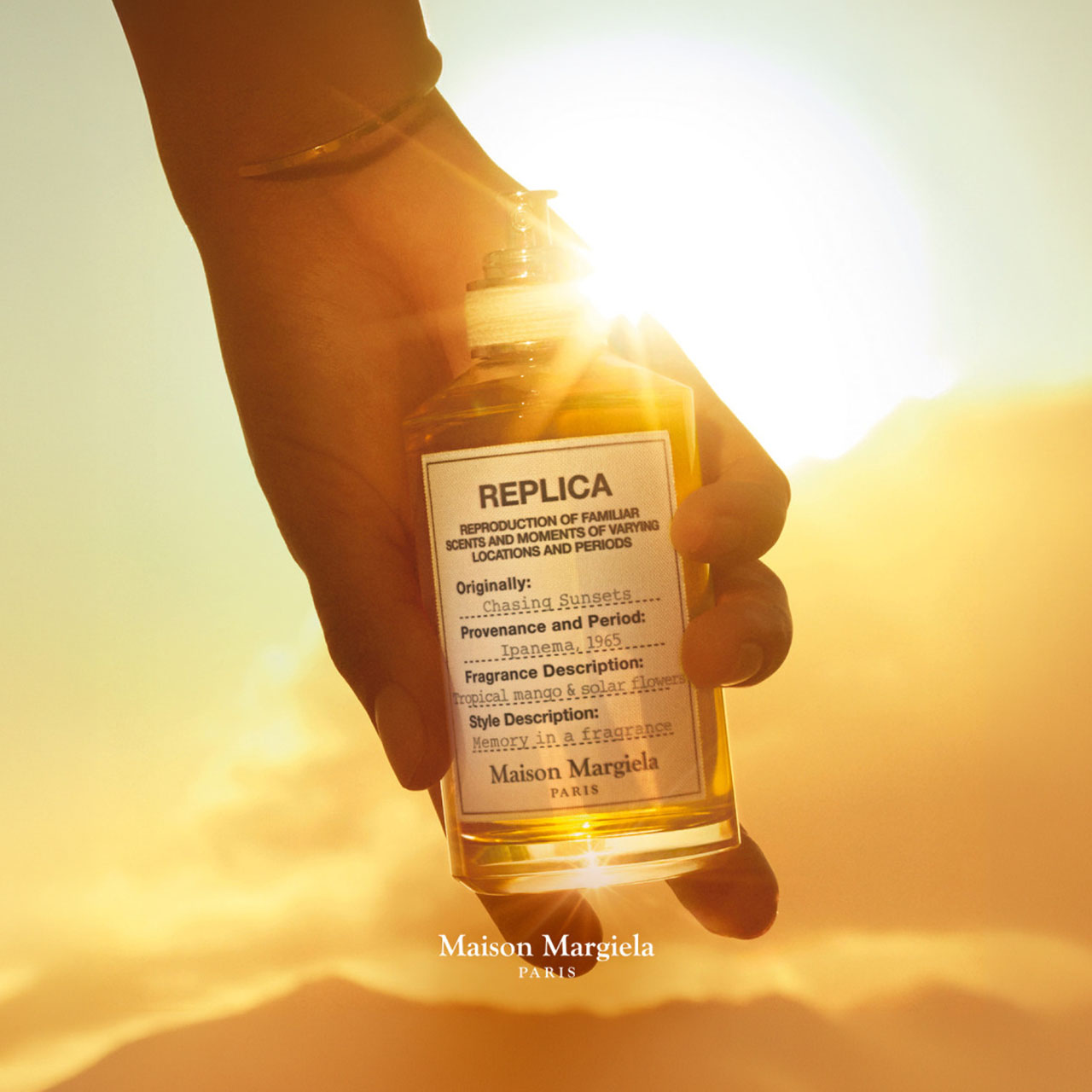 Maison Margiela Replica fragrance bottle held against golden sunlit background, with product label visible