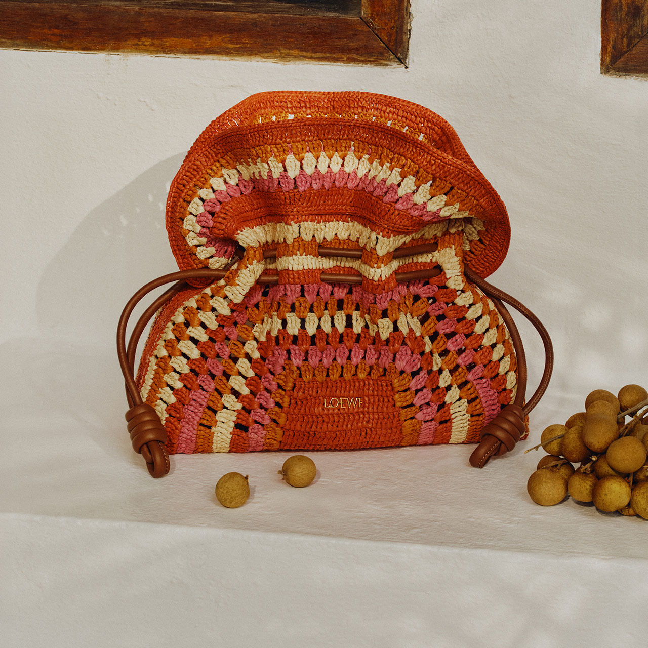 A colorful, woven handbag with a drawstring design, accompanied by small, round fruits on a white surface.