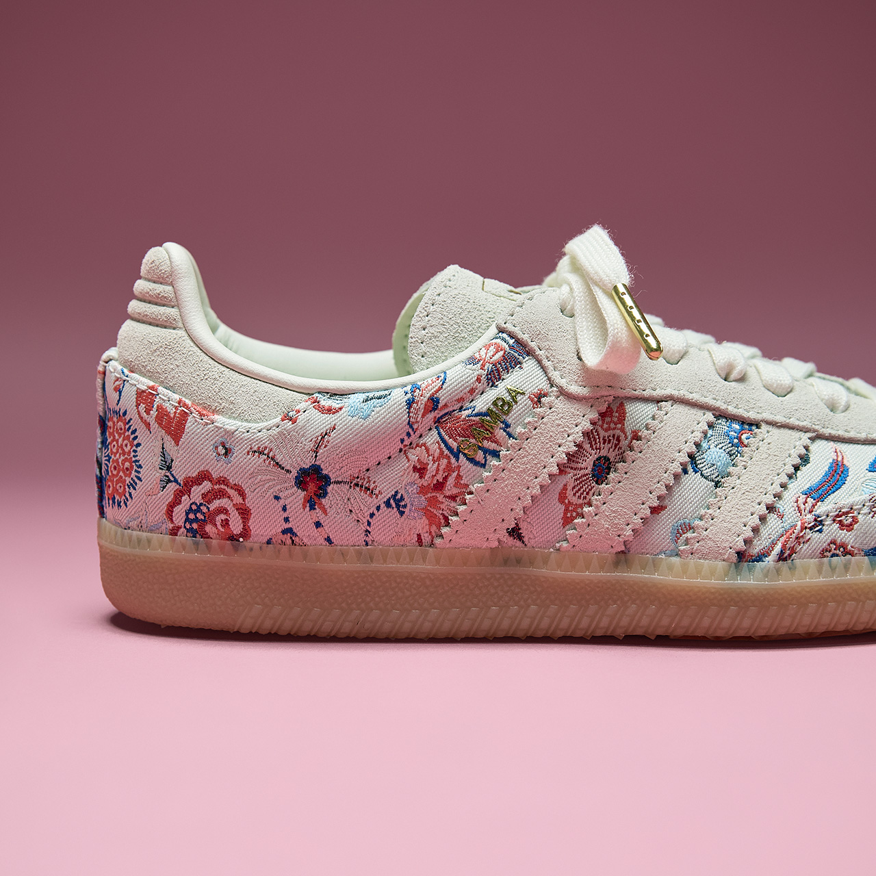 White suede trainer with floral patterned fabric panel and cream rubber sole on pink background