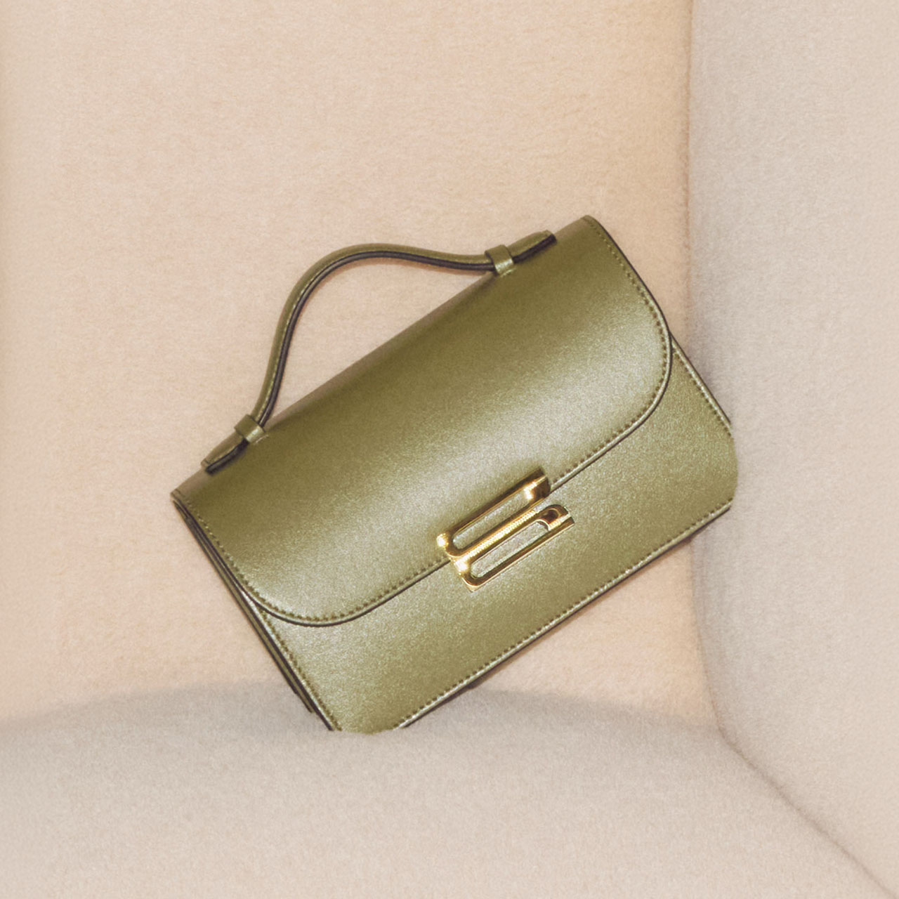 Olive green leather shoulder bag with gold clasp and adjustable strap on neutral background
