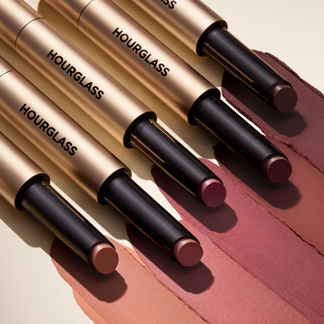 Range of Hourglass lipstick tubes with black and gold packaging displayed diagonally on mauve-toned swatches
