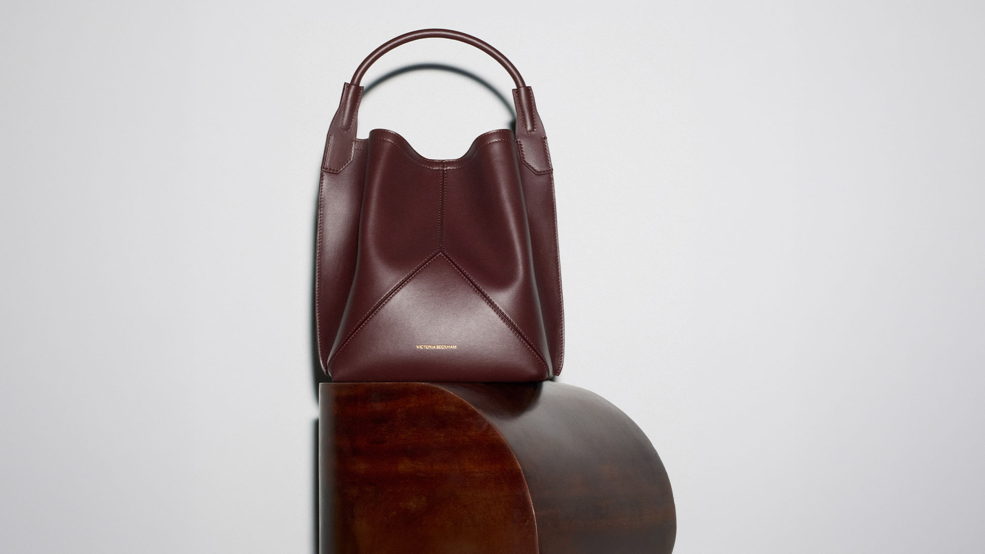Burgundy leather hobo handbag with handles displayed on wooden circular platform