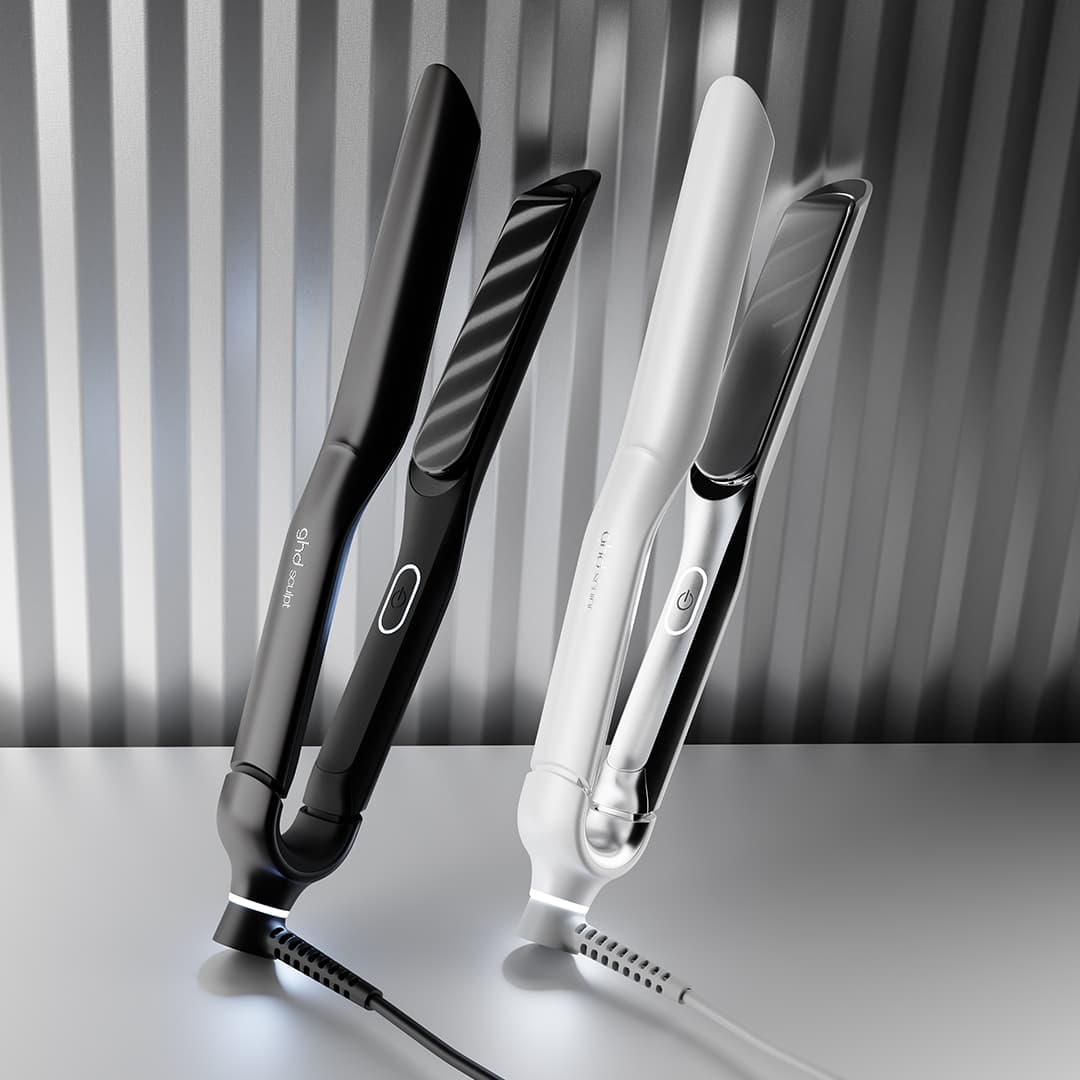 Two sleek hair straighteners, one in black and the other in white, are positioned upright on a reflective surface. They feature modern designs with illuminated power indicators. The background has a metallic, vertically striped pattern, enhancing their stylish appearance.
