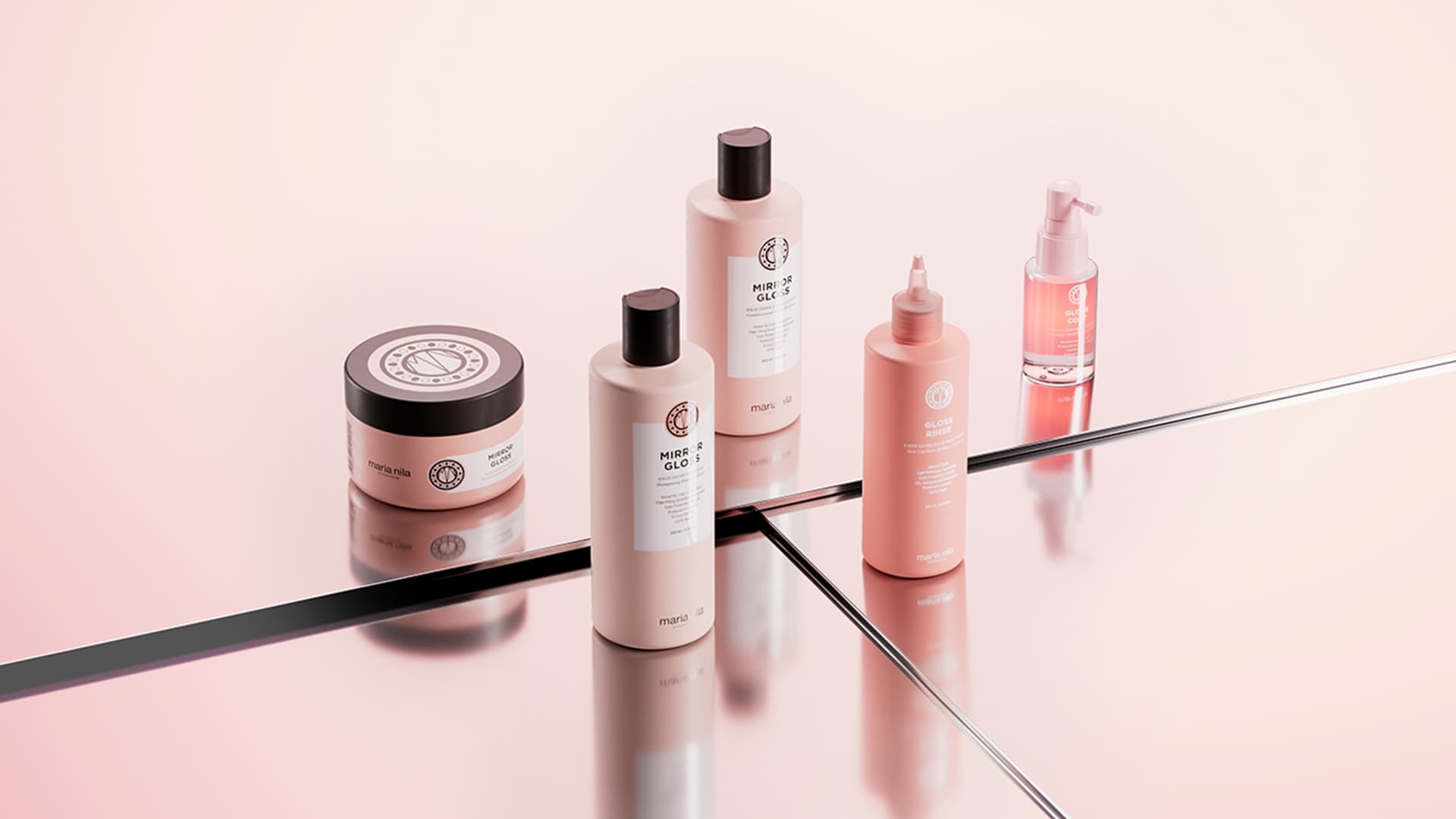 A collection of beauty products arranged on a reflective pink surface. The set includes bottles with black and pink caps, a jar, and a small pump bottle. Each product features similar branding and labels, suggesting a coordinated skincare or haircare line.