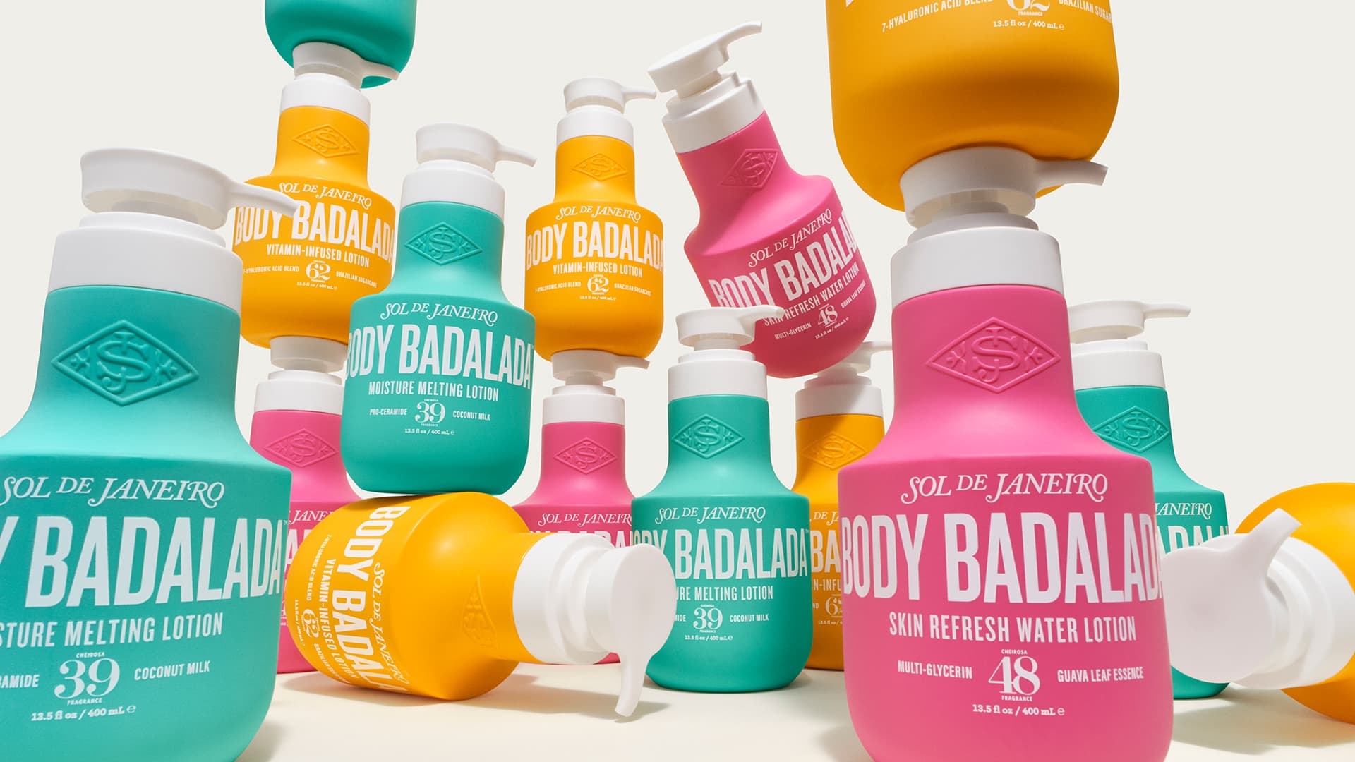 Various colourful bottles of Sol de Janeiro Body Badala lotions are arranged together. The bottles are in vibrant shades of pink, turquoise, and yellow, each featuring bold white text describing the product. The design is striking and modern, highlighting skincare items.