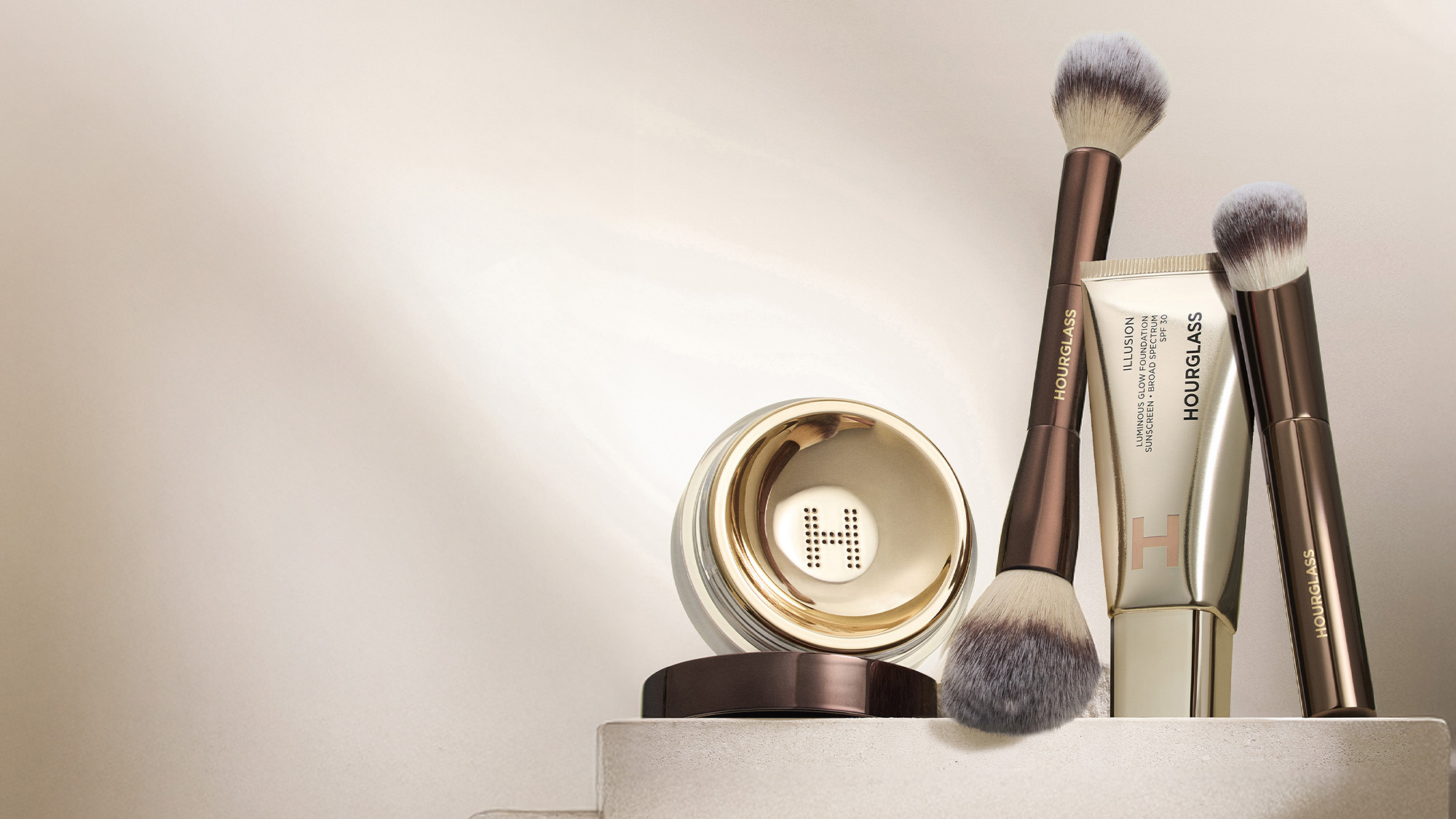 Makeup set with brushes, a tube, and a round compact, all in elegant packaging.
