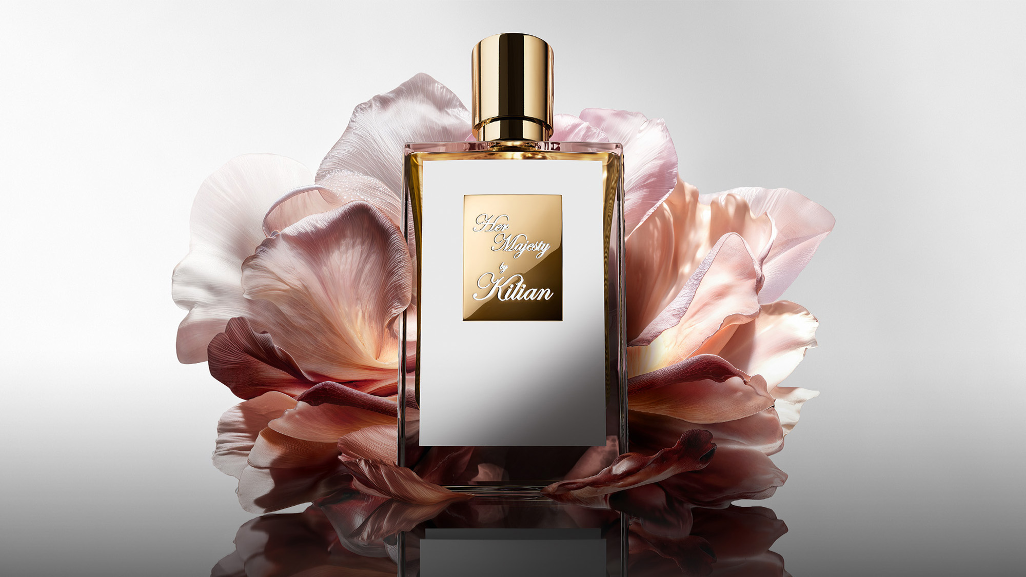 A perfume bottle with a gold cap and label is surrounded by soft pink petals.