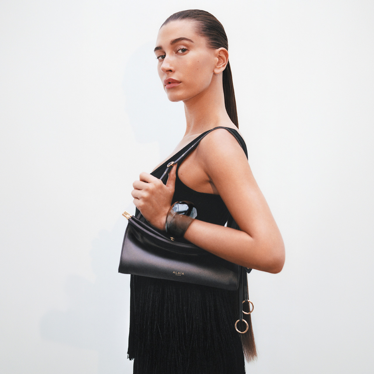 Woman wearing black sleeveless dress holding black shoulder bag with fringe detail