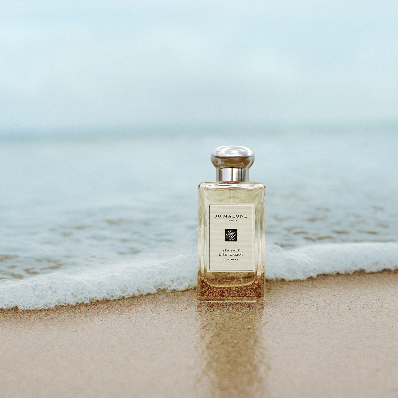 Jo Malone Sea Salt and Bergamot cologne bottle positioned on sandy beach with ocean waves in background