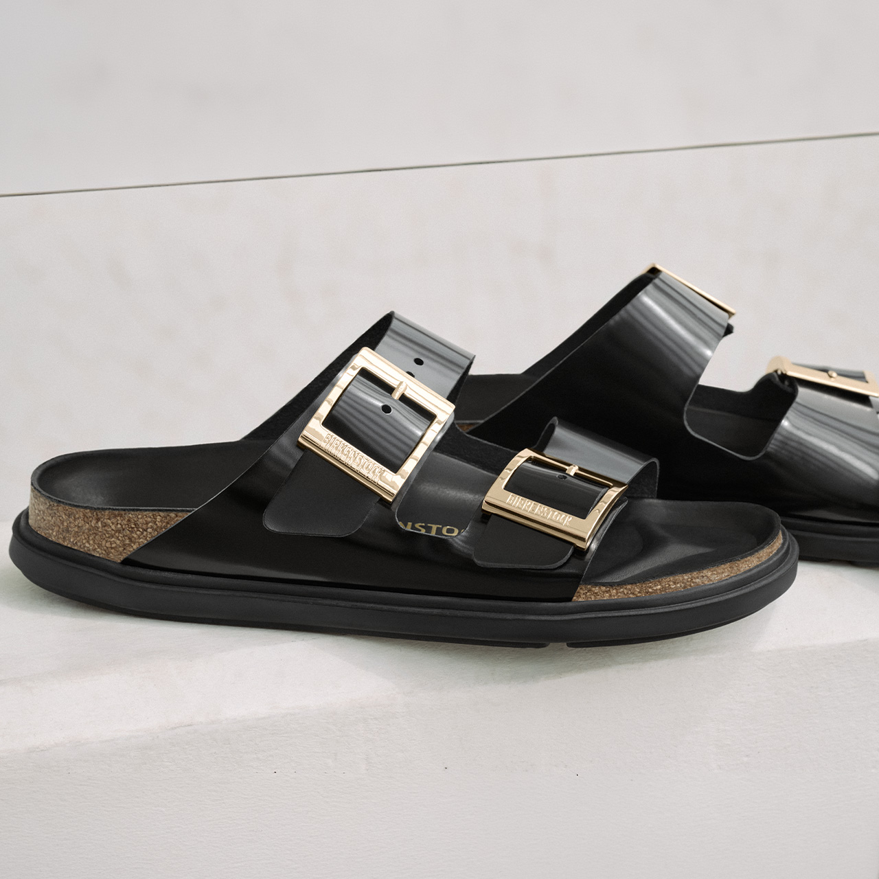 Black leather Birkenstock sandals with dual gold buckle straps and cork footbed