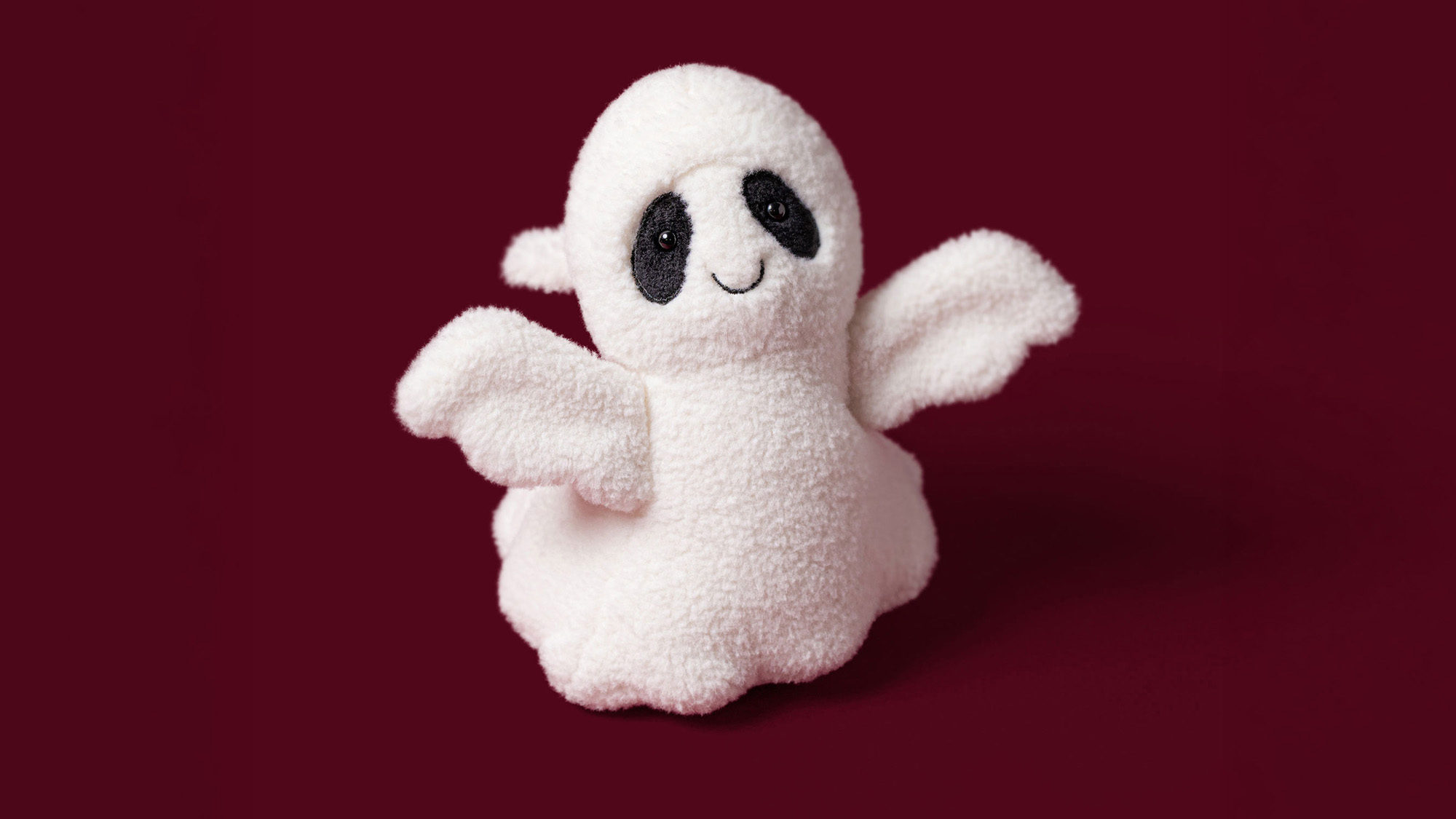 White fluffy ghost plush toy with black eyes and smile on burgundy background