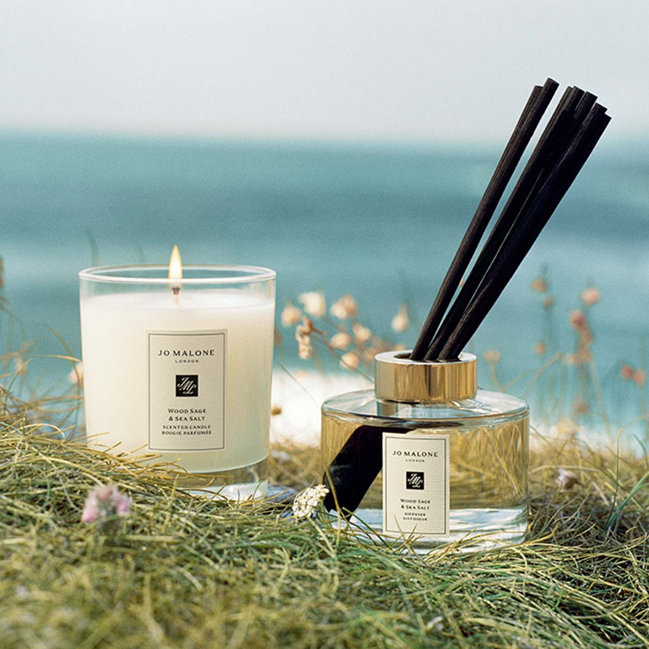 Jo Malone London scented candle and diffuser displayed on sand with sea and dried grasses backdrop