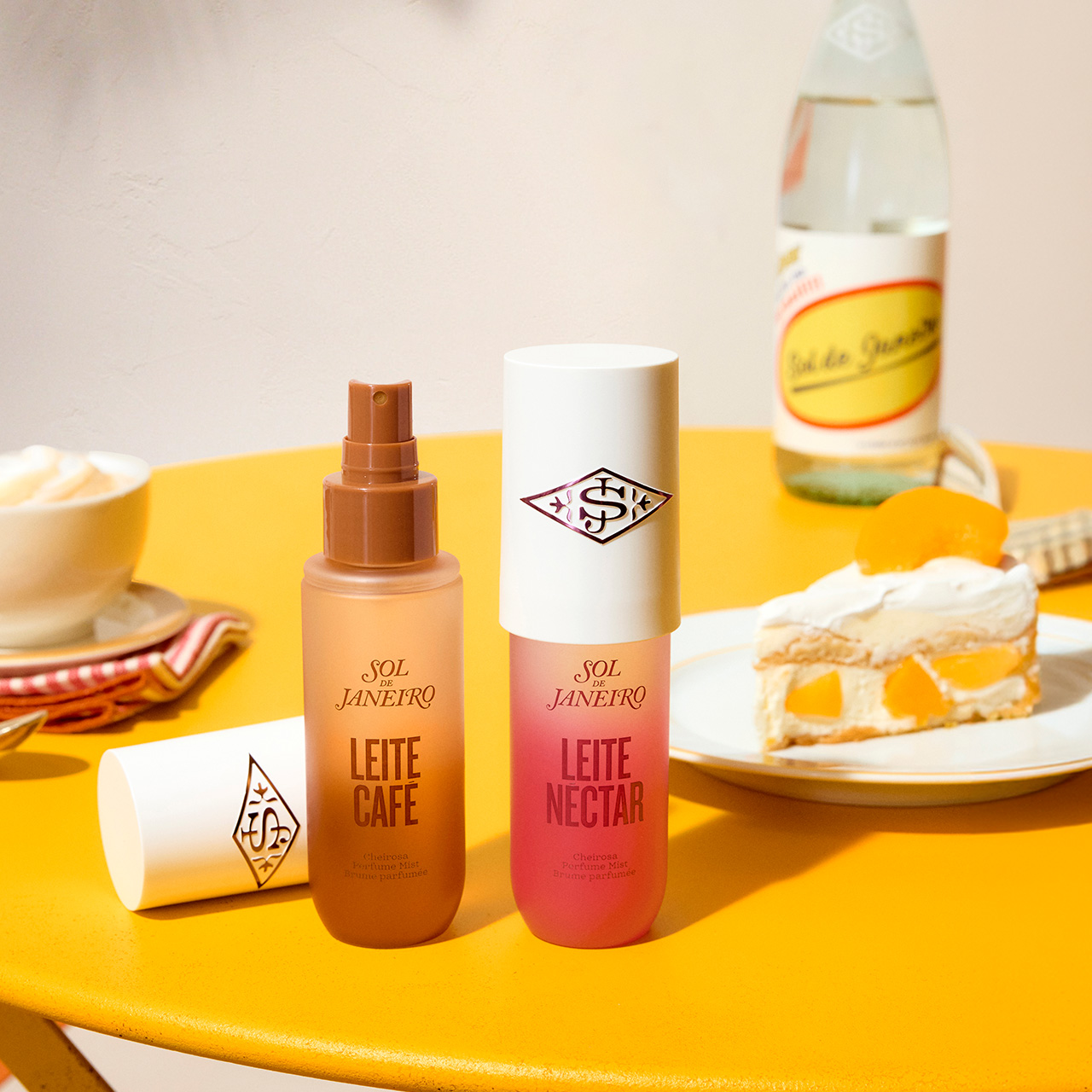 Sol De Janeiro Leite perfume mists in latte and peach scents displayed on a yellow table with coffee and desserts