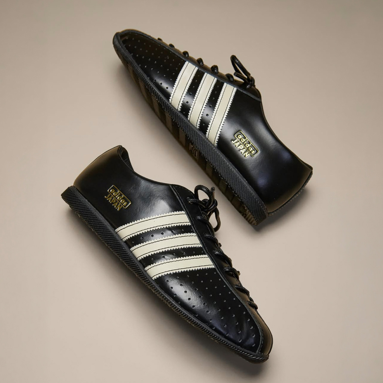 Two black leather shoes with white striped detailing on neutral background