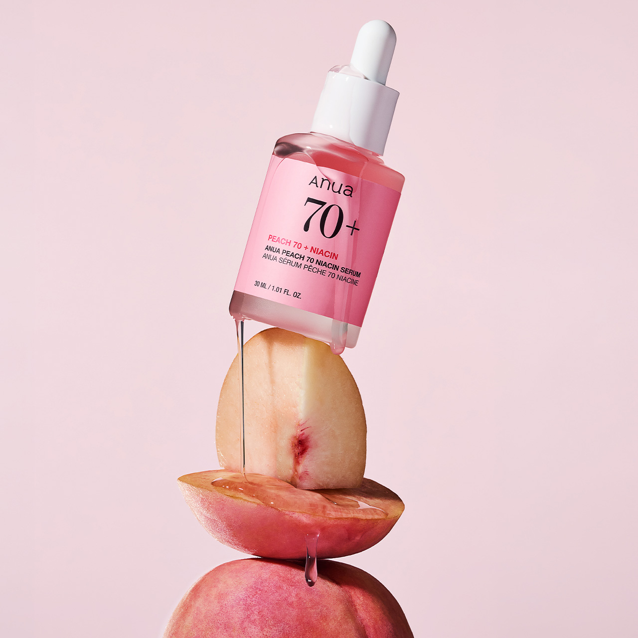 Anua Peach 70+ Niacin serum bottle dripping onto fresh peach and apple slices against pink background