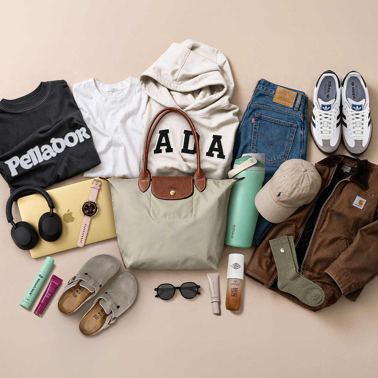 Flatlay of back-to-college essentials including trainers, jeans, graphic hoodies, brown jacket, cream handbag, headphones, smartwatch, sunglasses, cap and beauty products