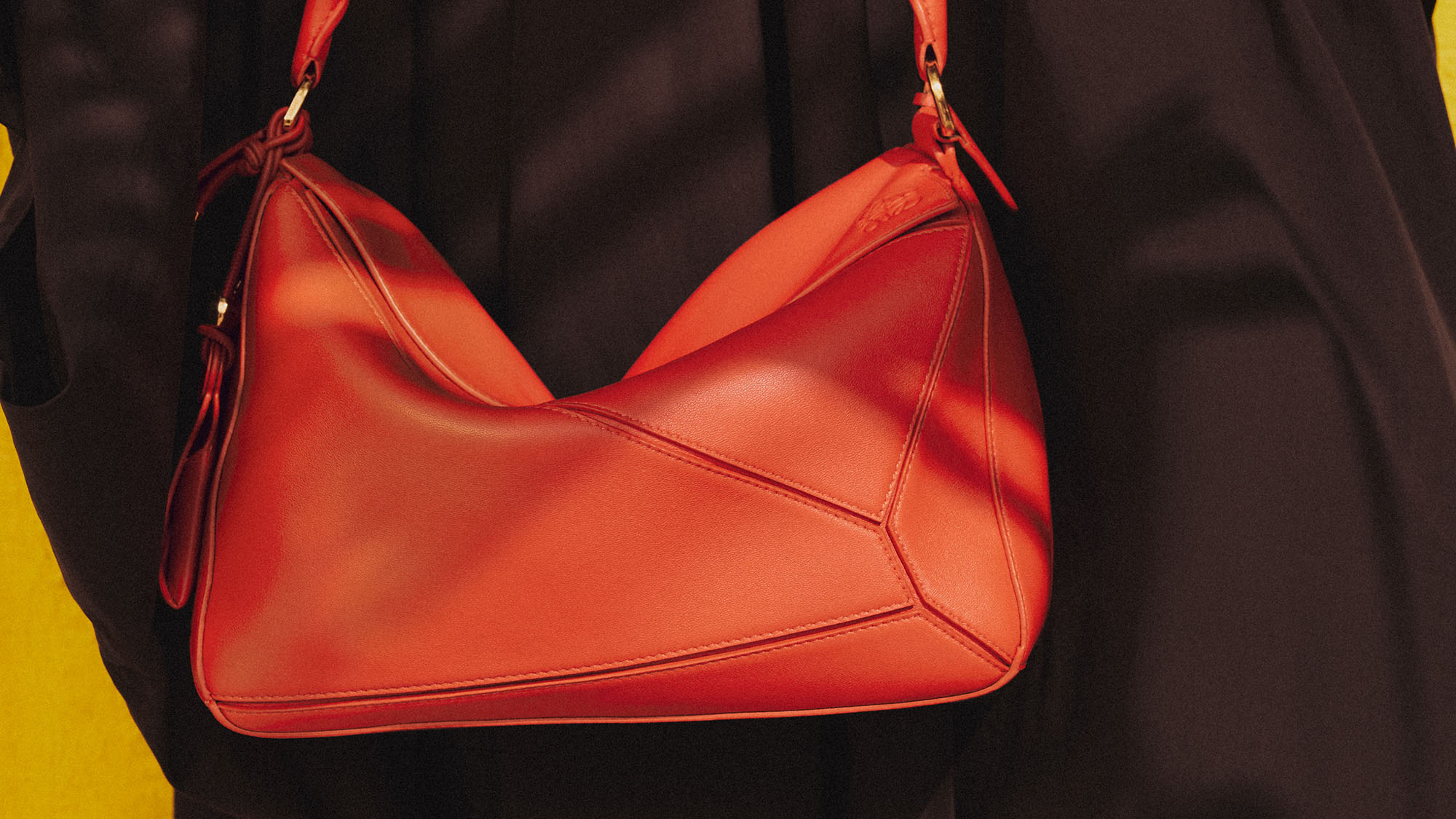 Bright red leather shoulder bag with curved silhouette and dual straps held against dark background
