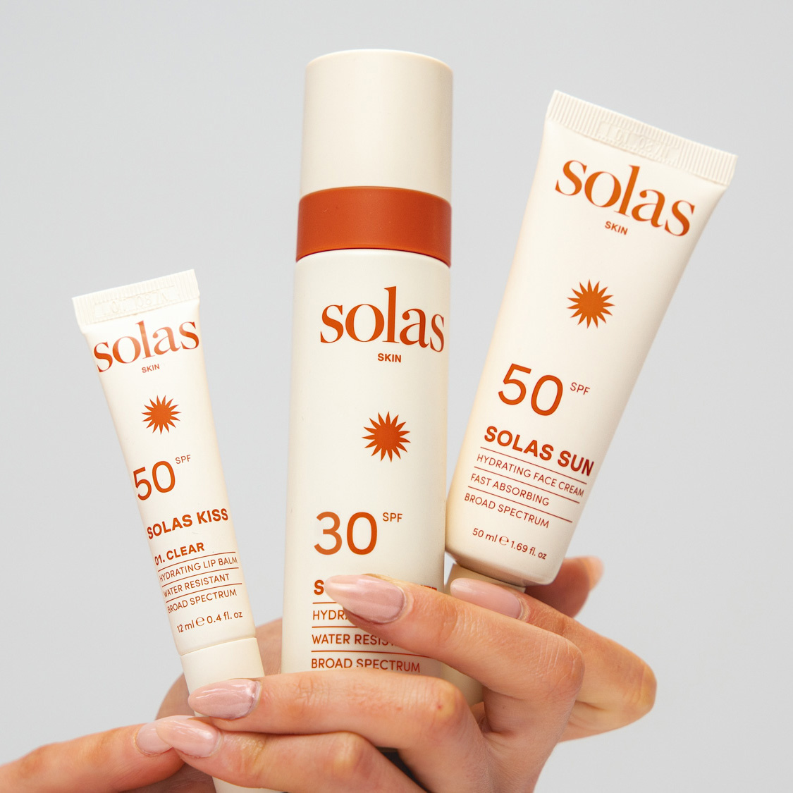 Hand holding three Solas Skin sunscreen products with SPF 30 and SPF 50 protection against neutral background.