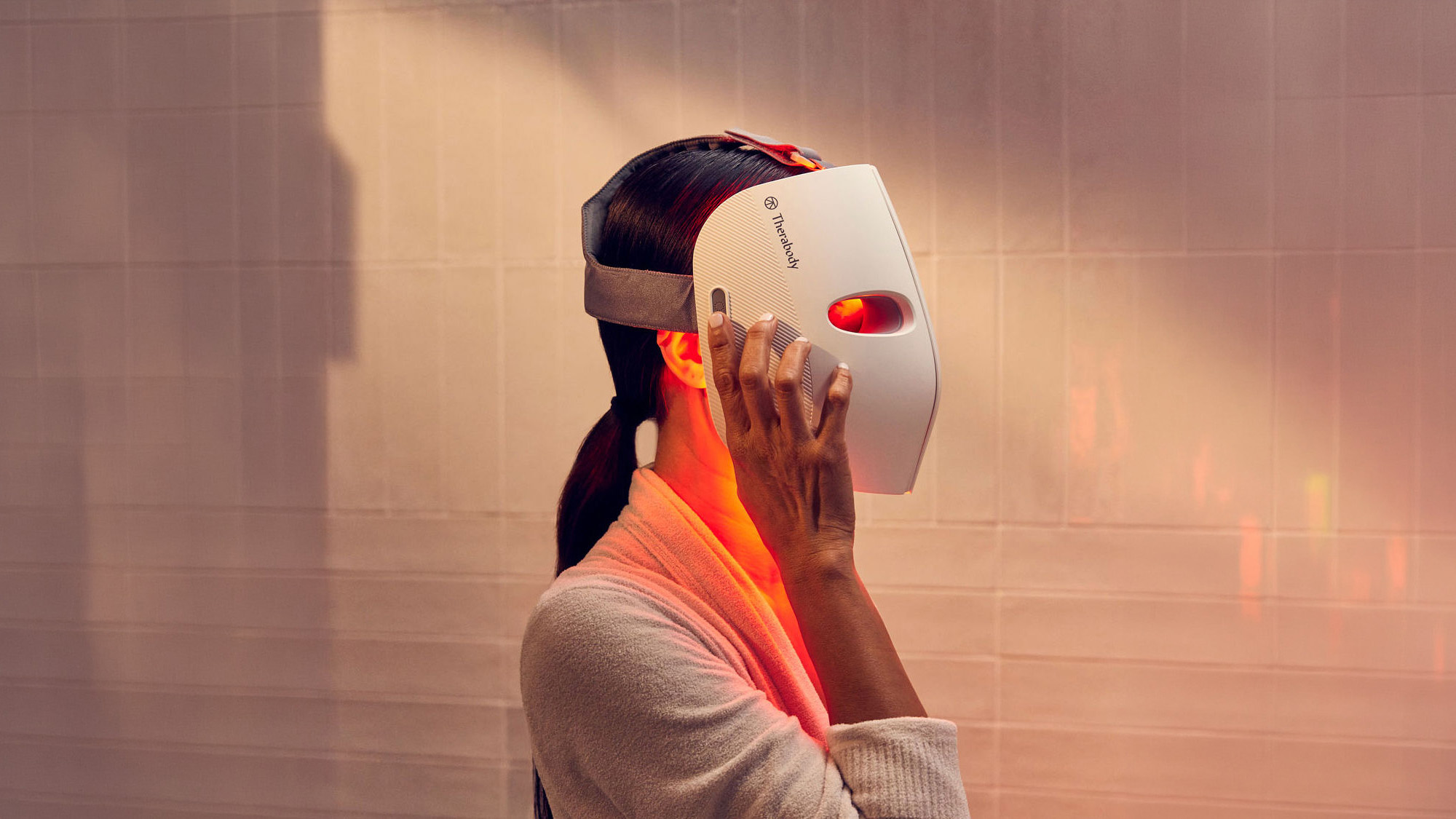Person using white Therabody facial device with red light therapy on neck and shoulder area