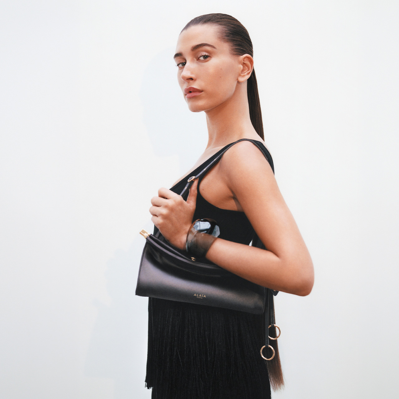 Woman in black tank top holding black leather shoulder bag with fringe detail