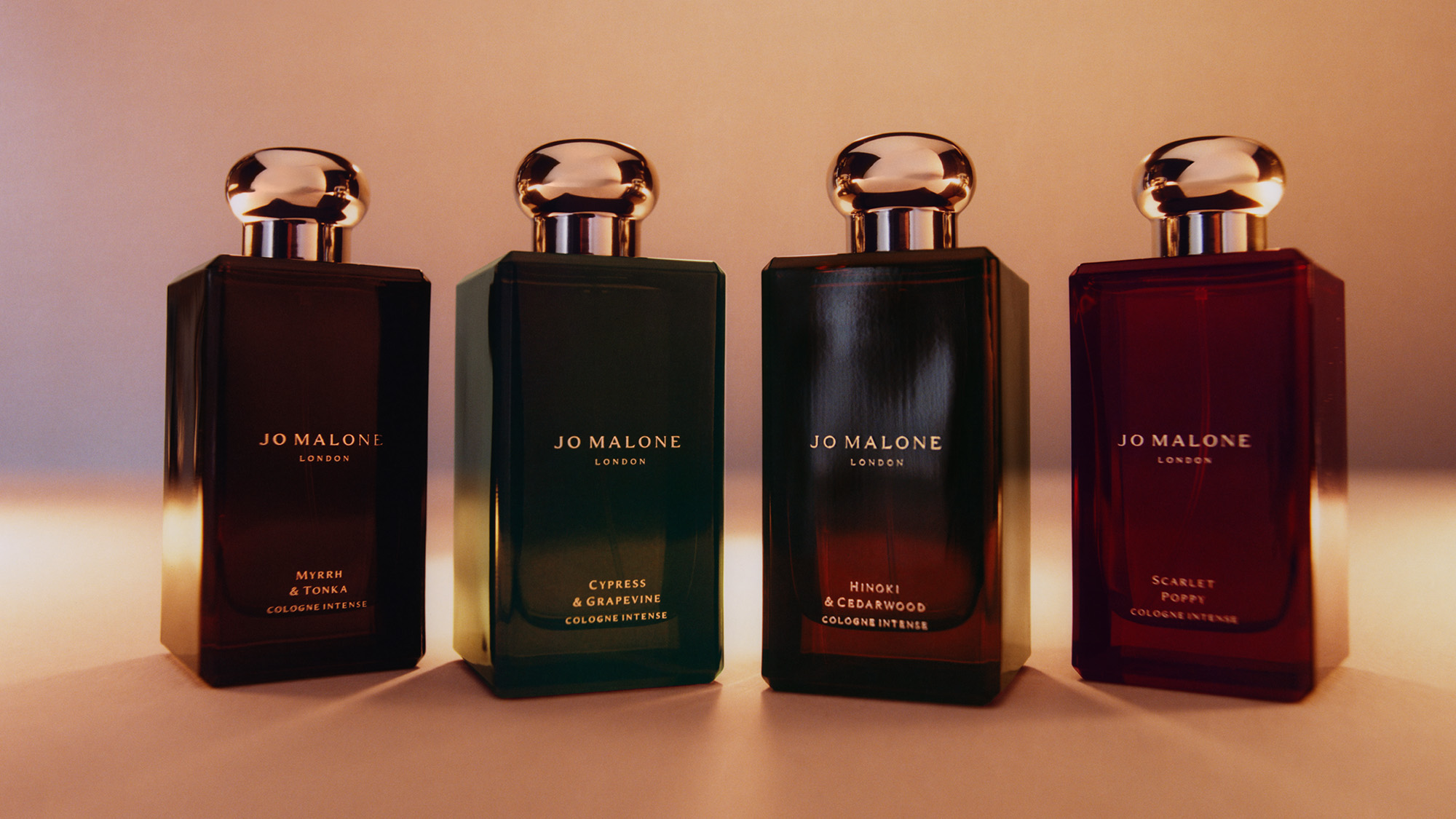 Four Jo Malone London Cologne Intense bottles in amber glass with rose gold caps, featuring Myrrh & Tonka, Cypress & Grapevine, Hinoki & Cedarwood, and Scarlet Poppy fragrances