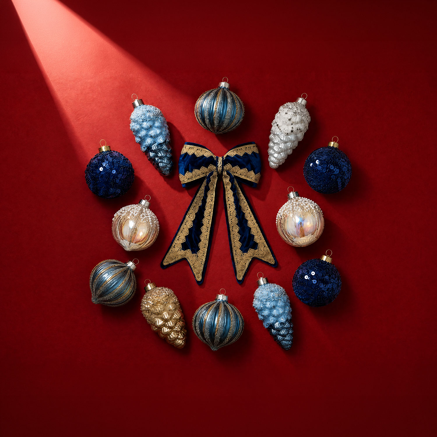 Alpine Christmas ornaments arranged in circle: navy and silver sequin baubles, light blue pinecones, white berries, and a navy and gold ribbon bow