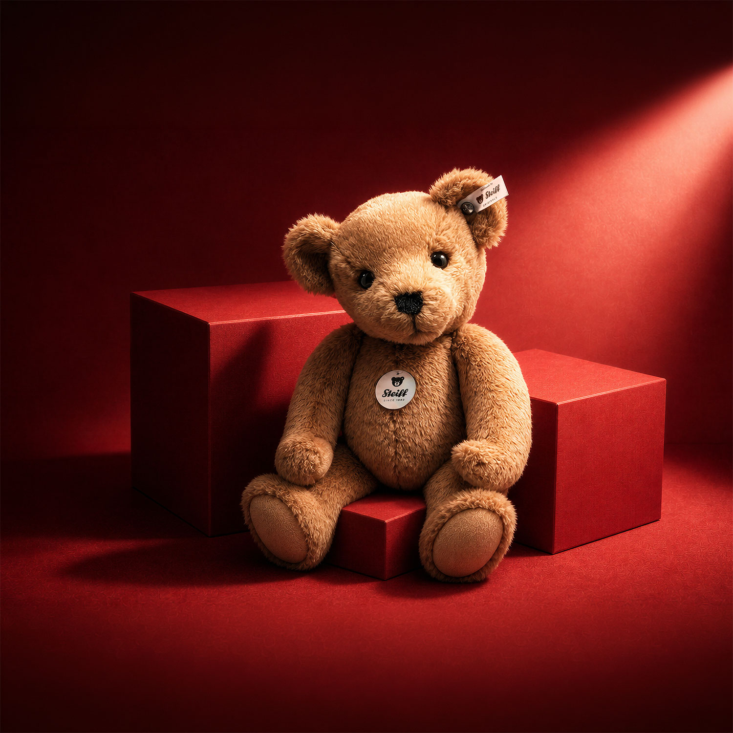 Tan teddy bear with Steiff label sitting on red geometric blocks against red background
