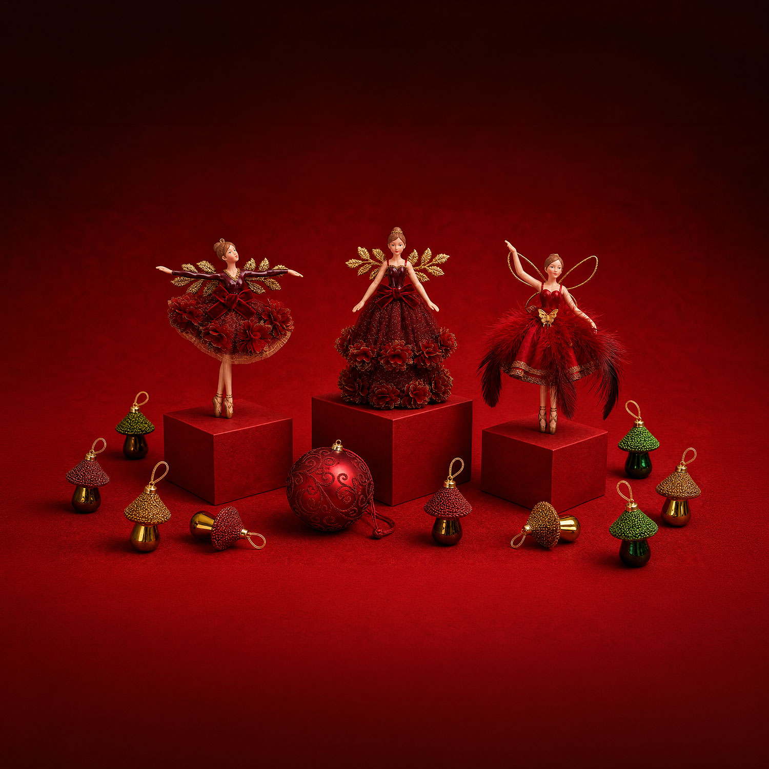 Three festive fairy figurines with gold wings in red dresses displayed on red blocks, surrounded by red and gold beaded bell ornaments