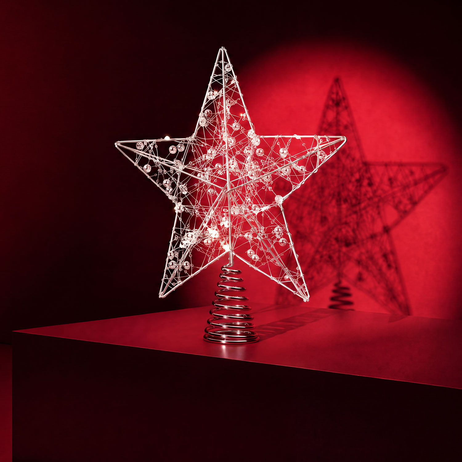White wireframe star Christmas tree topper with decorative baubles, set against red background with glowing effect