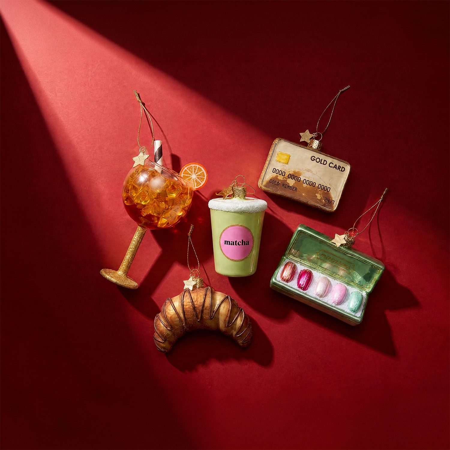 Novelty Christmas ornaments including gold cocktail glass, matcha latte cup, gold credit card, nail polish palette and croissant decoration