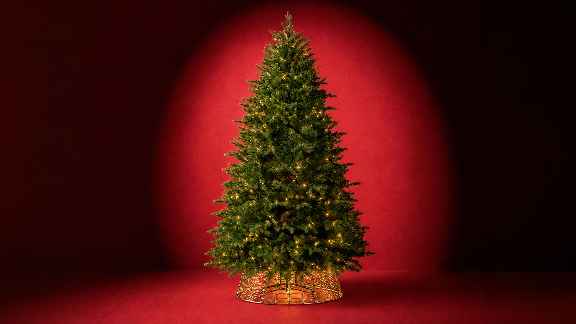 Illuminated artificial Christmas tree with warm white lights and gold woven base against red background