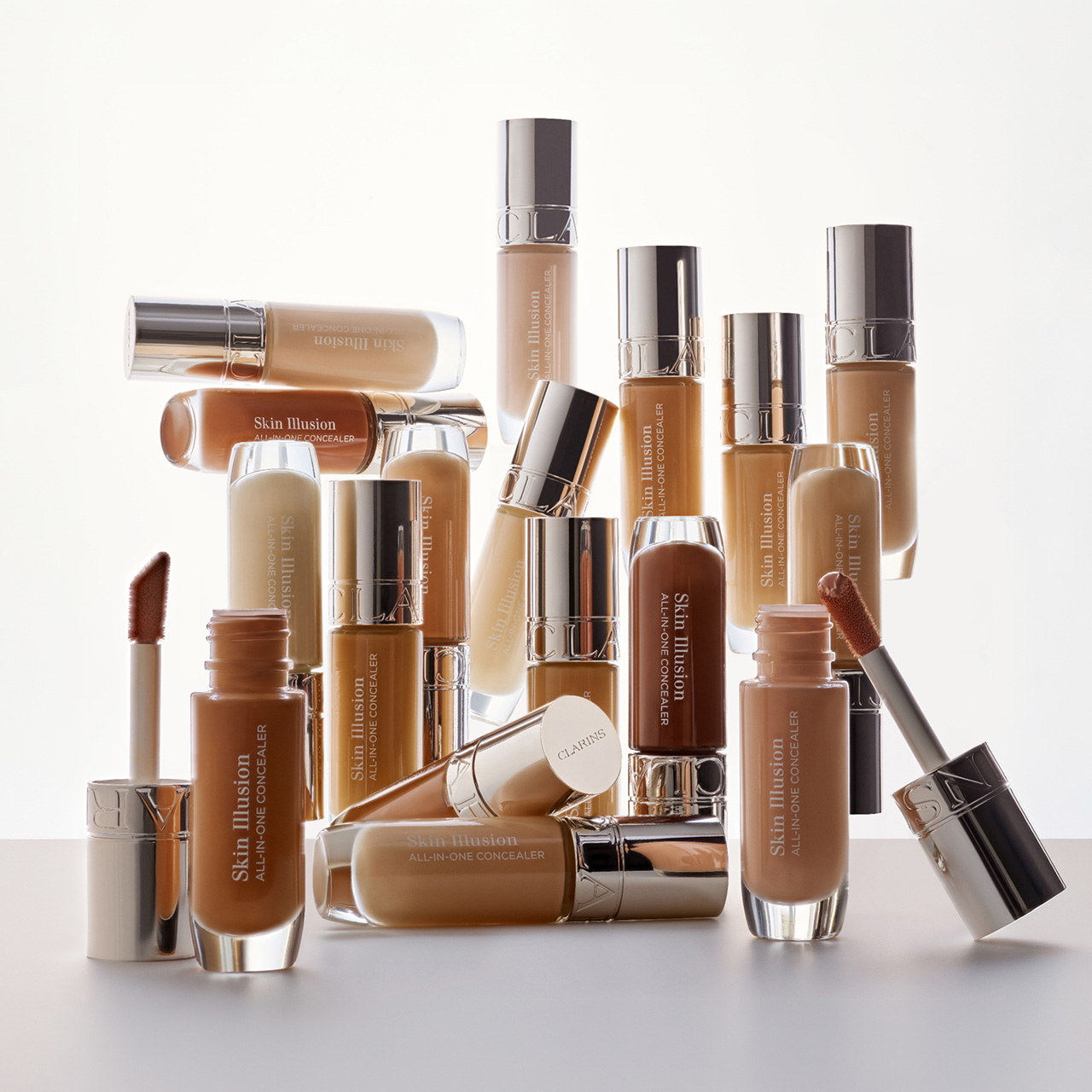 Collection of Clarins foundation, concealer, and lip products in various nude and brown tones, arranged on white surface