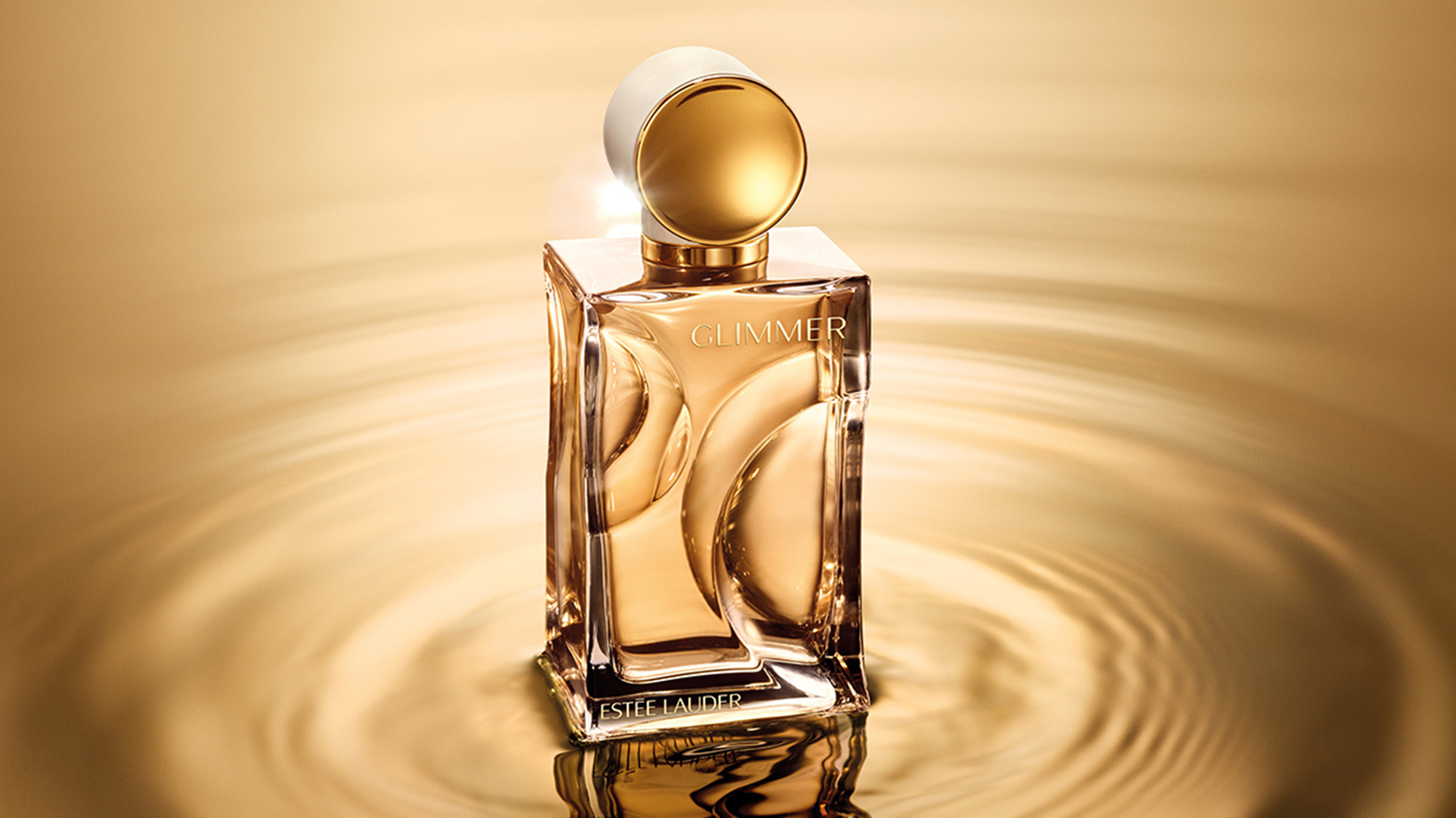 Estée Lauder Glimmer fragrance bottle with gold liquid and spherical stopper, centred with golden light rays