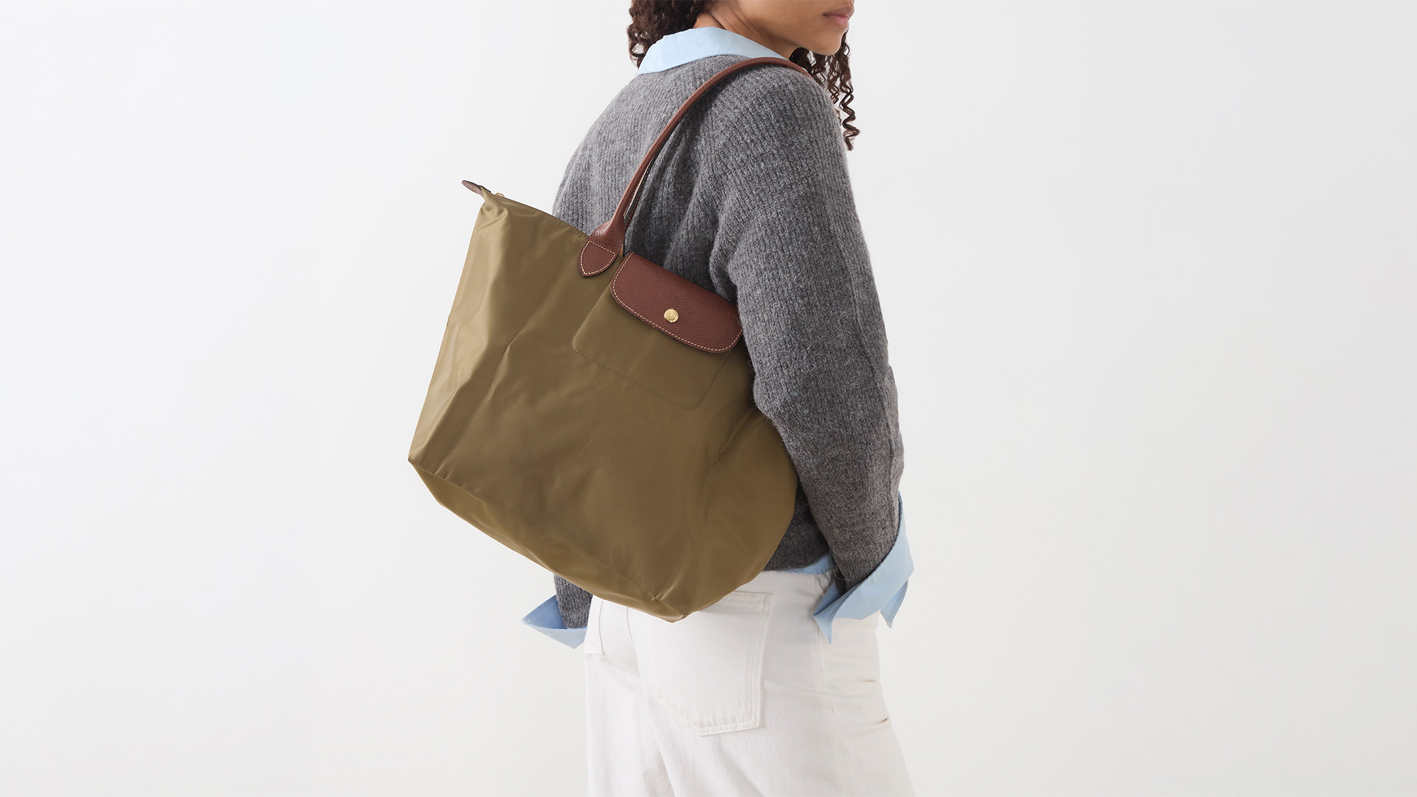 Woman wearing grey knit and white jeans carrying olive green tote bag with brown handles