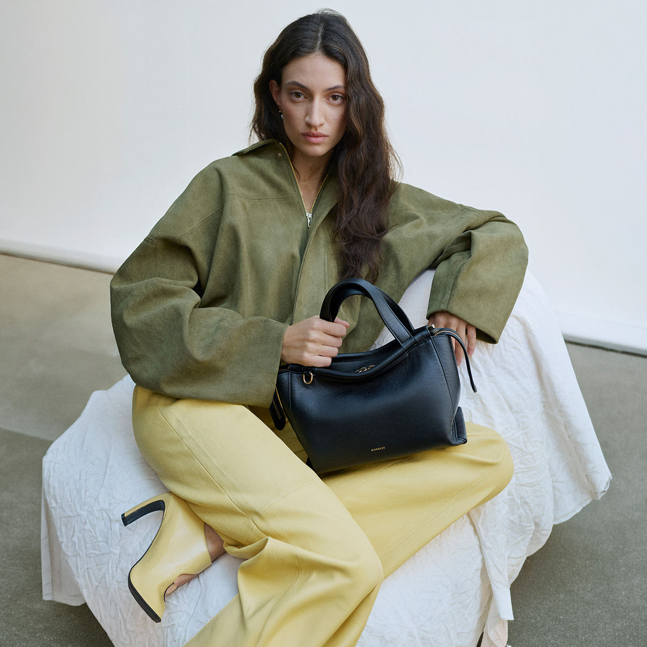 Woman wearing olive jacket and yellow trousers holding black leather handbag