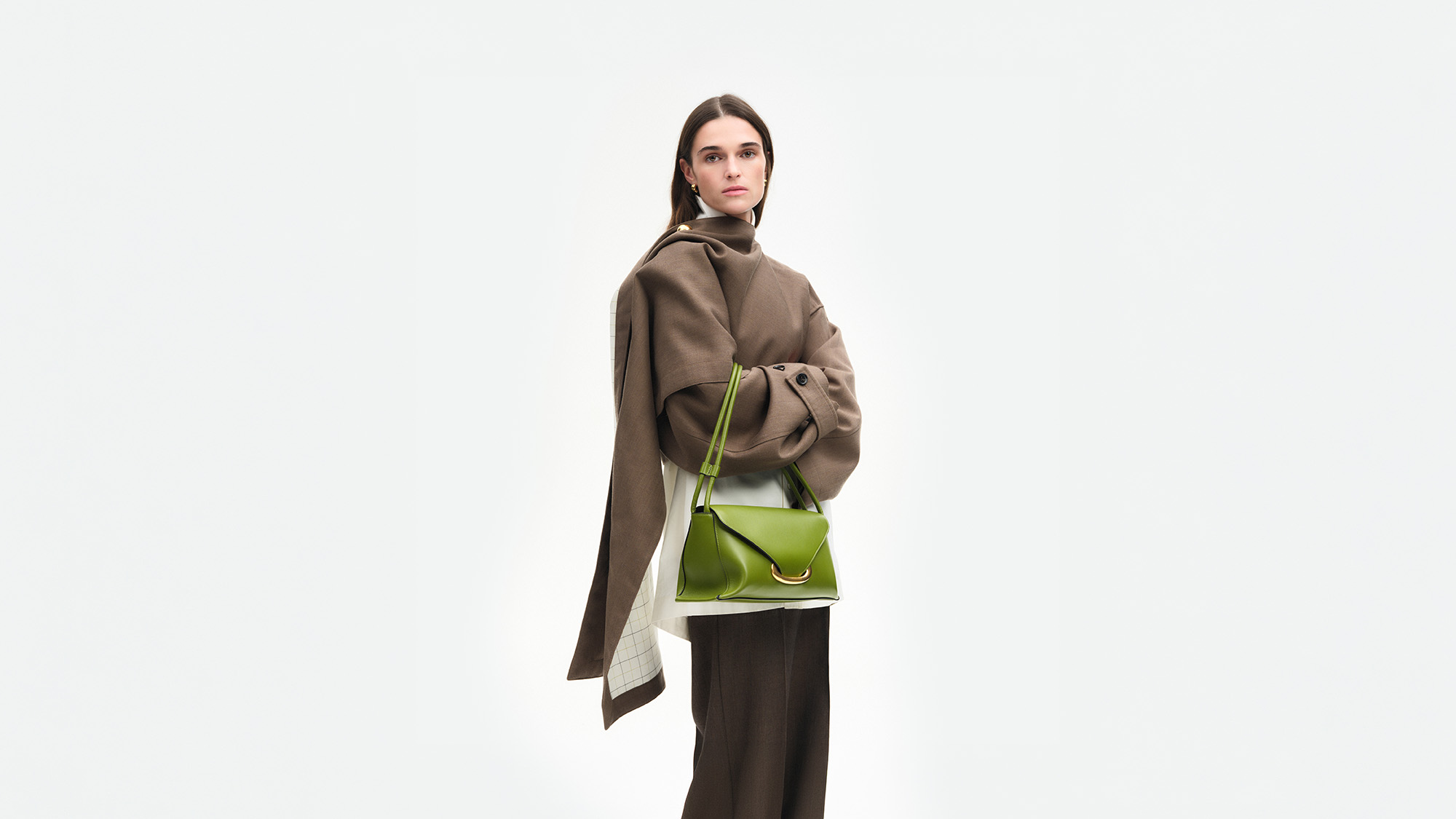 Woman wearing beige coat and black trousers with bright green leather shoulder bag