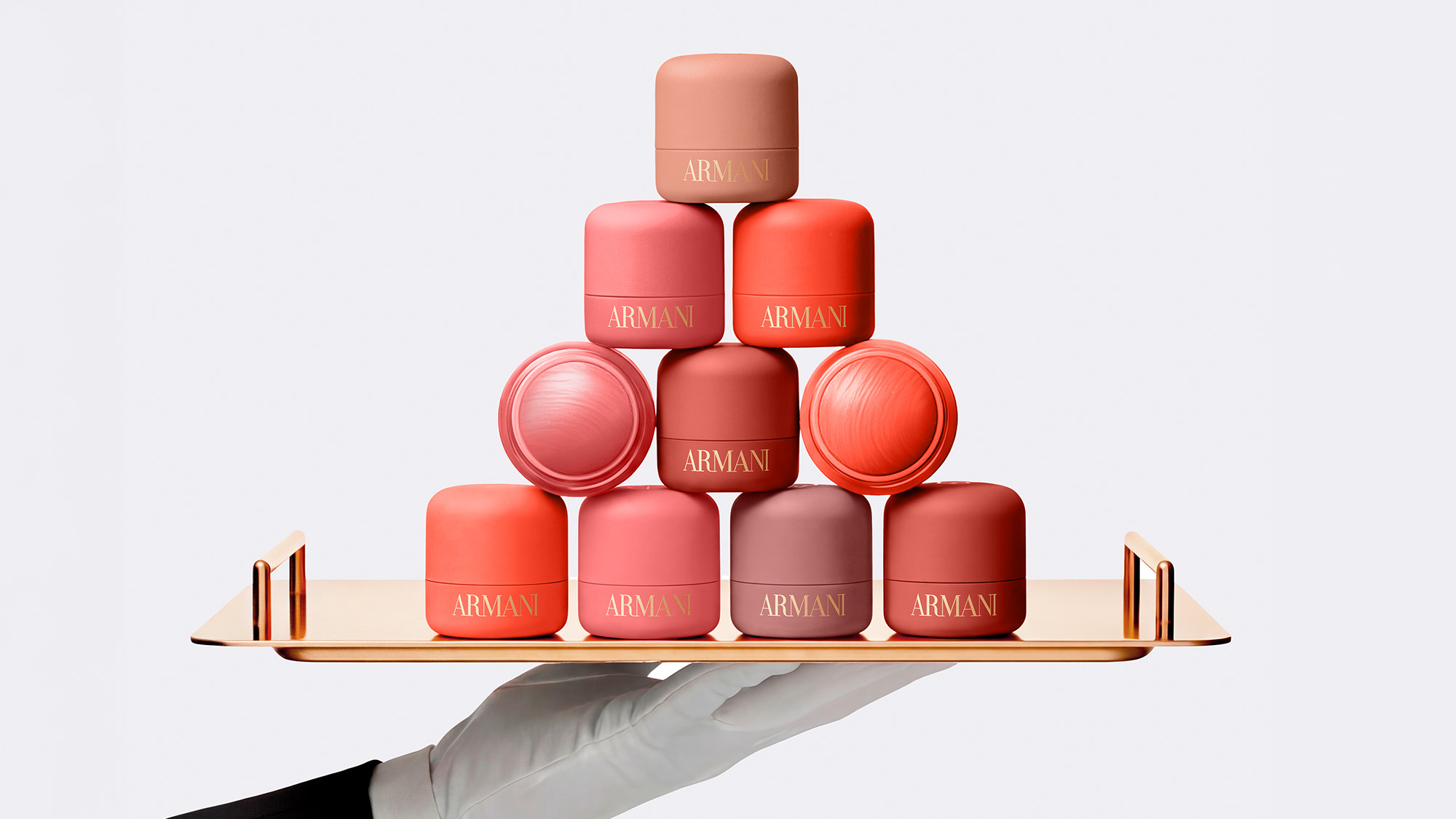 Pyramid display of Armani Beauty blush pots in various coral, pink and nude shades on a gold tray held by a gloved hand