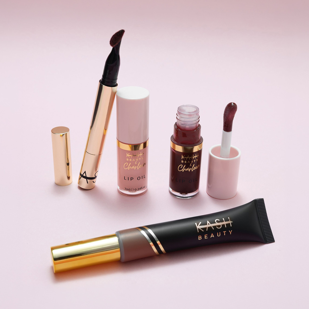 Kash Beauty X Charleen makeup collection featuring black eyeliner, nude lip oil, burgundy liquid lipstick, and brown lip tint with gold trim