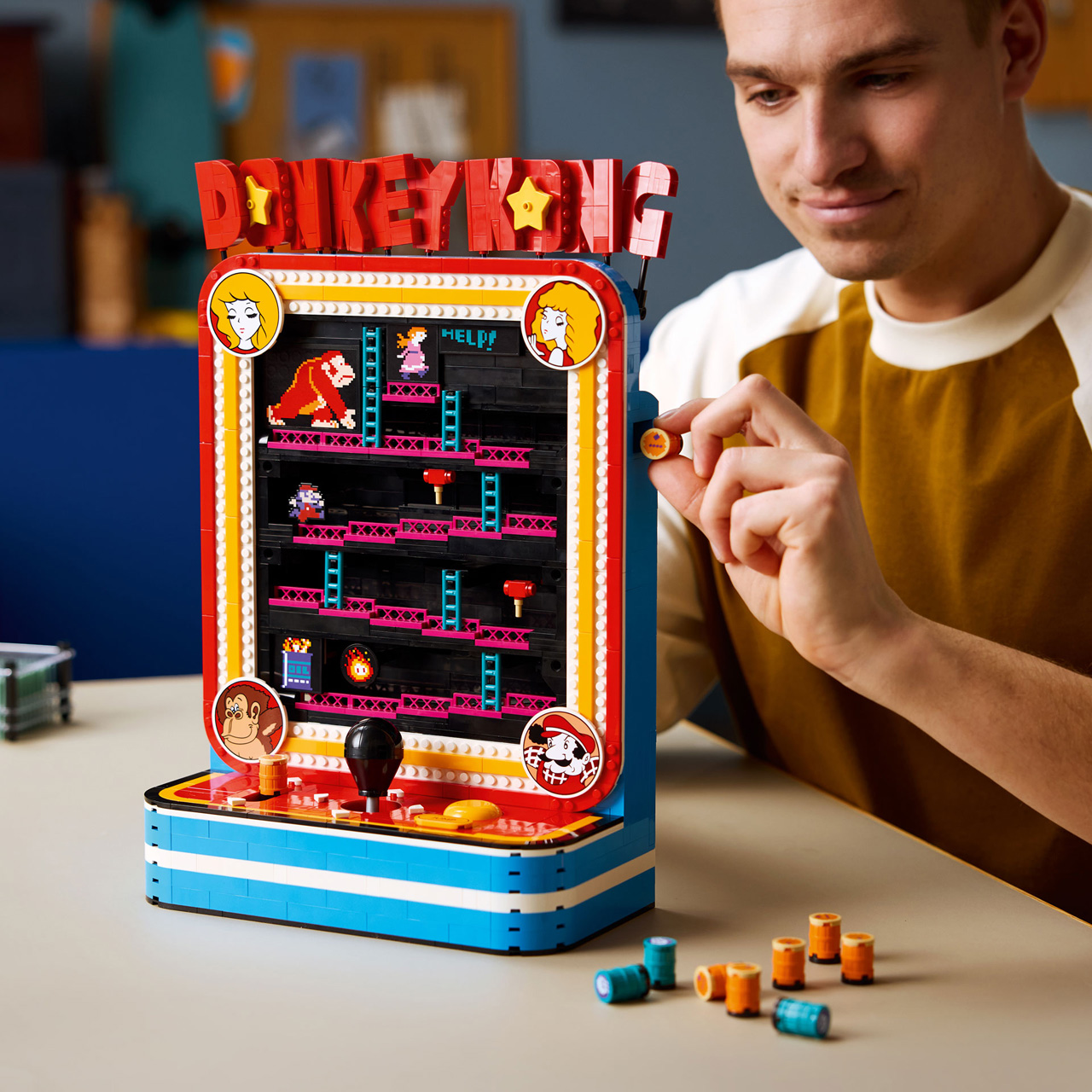 Man playing Donkey Kong arcade game set, a red and blue retro-style Lego building set with coloured brick pieces