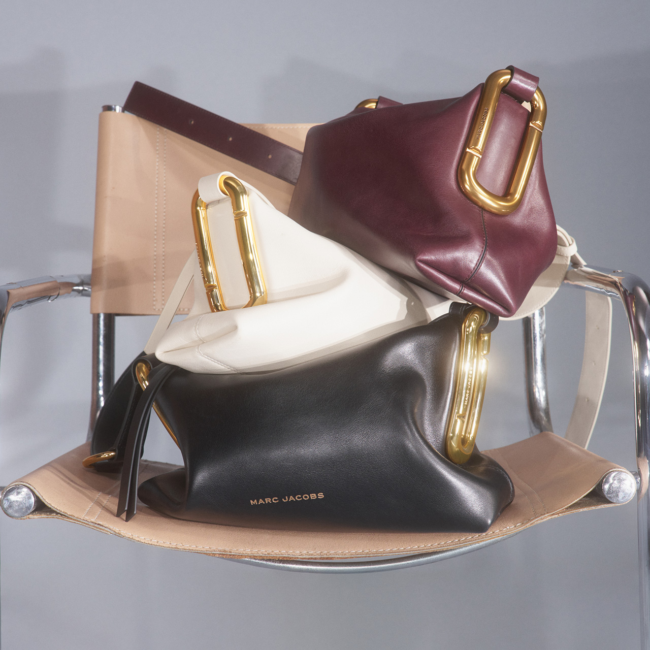 Collection of designer handbags in burgundy, cream, and black leather with gold hardware displayed on a chrome stand