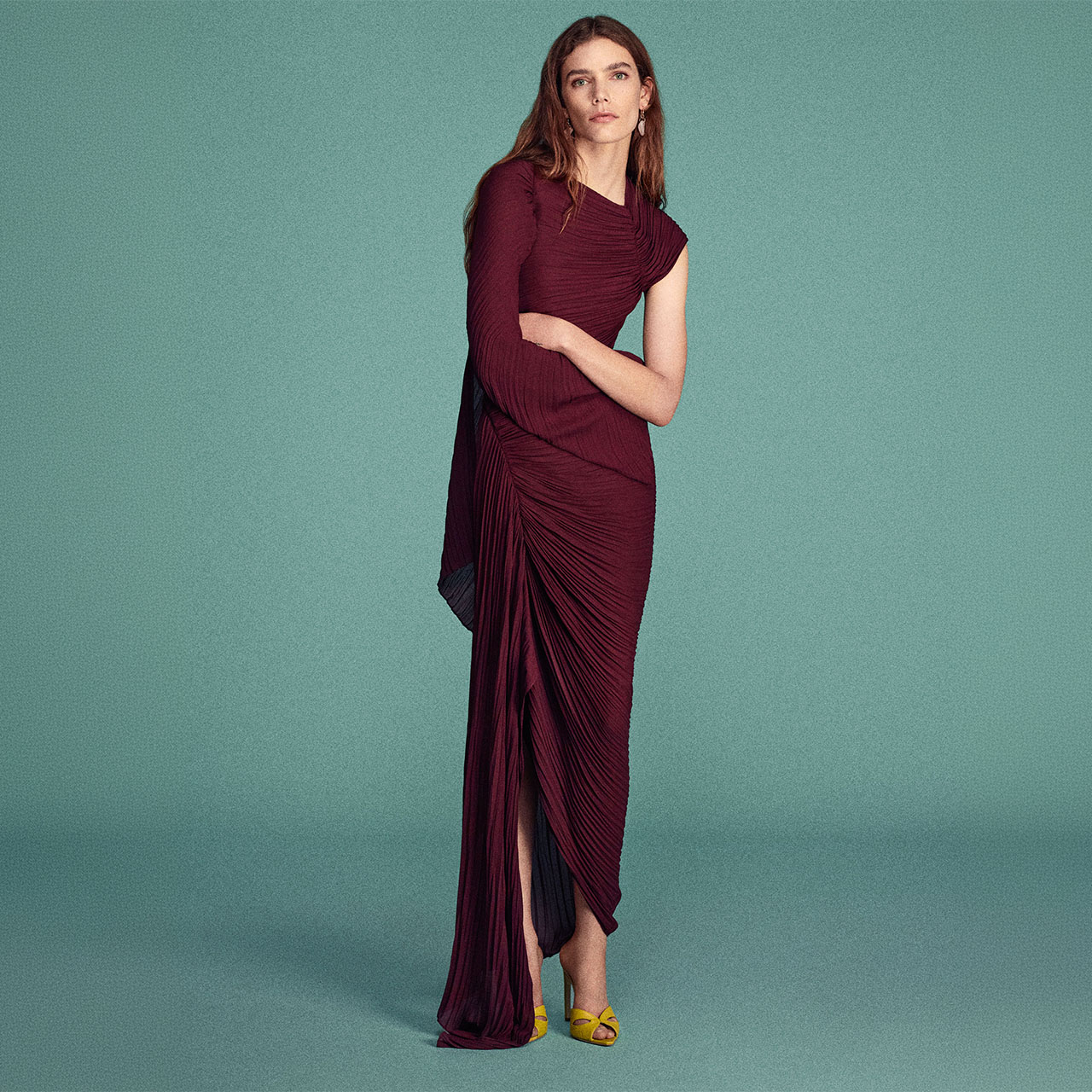 Woman in burgundy pleated midi dress with short sleeves against teal background