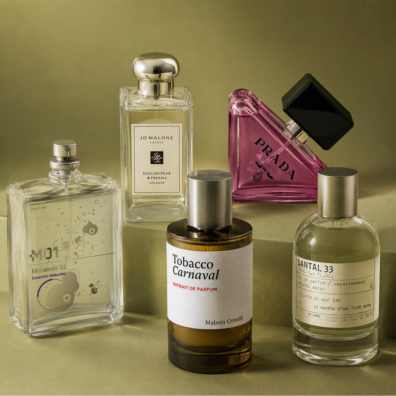 Collection of designer fragrances including Jo Malone, Prada, Maison Crivelli and Le Labo on olive background