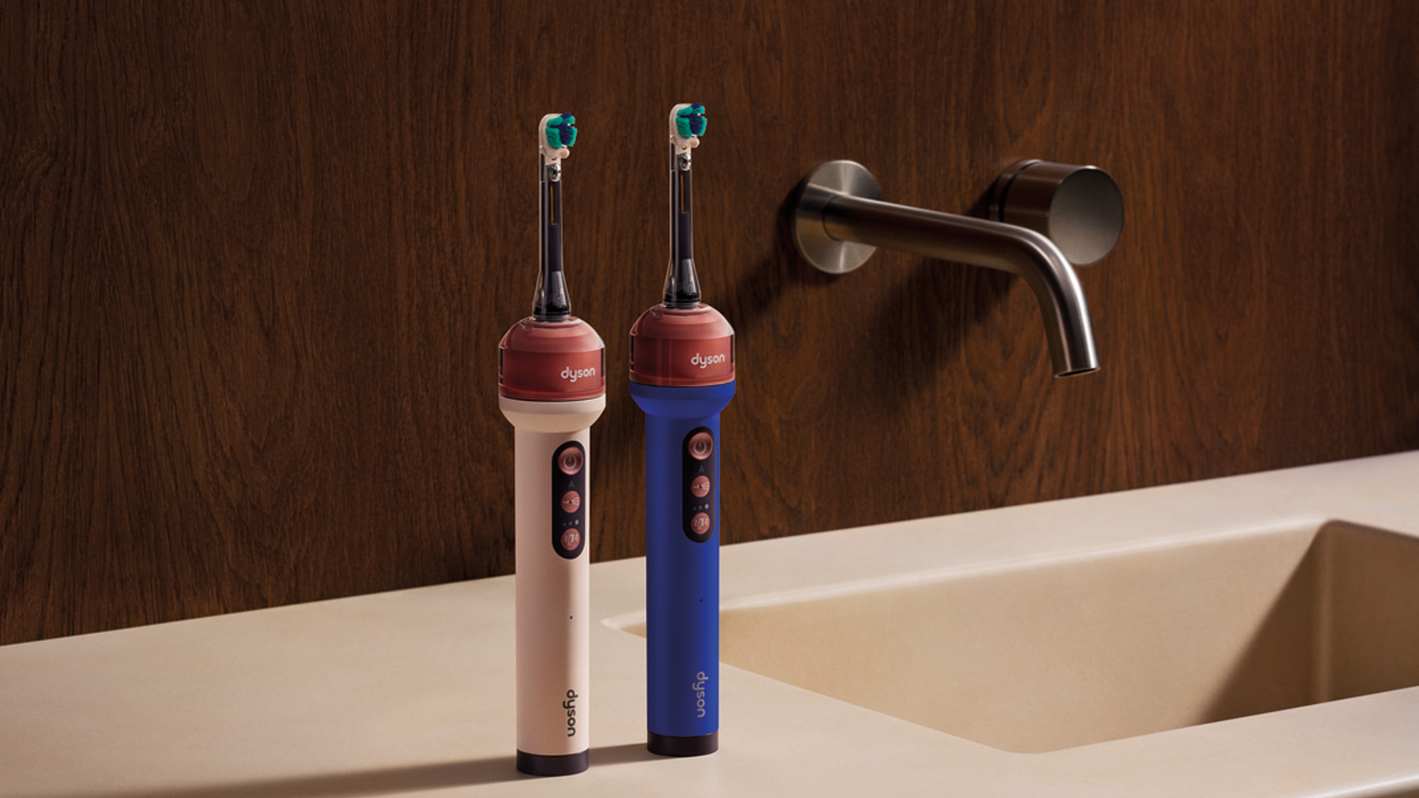 Two Dyson electric toothbrushes in cream and blue with teal brush heads on bathroom sink
