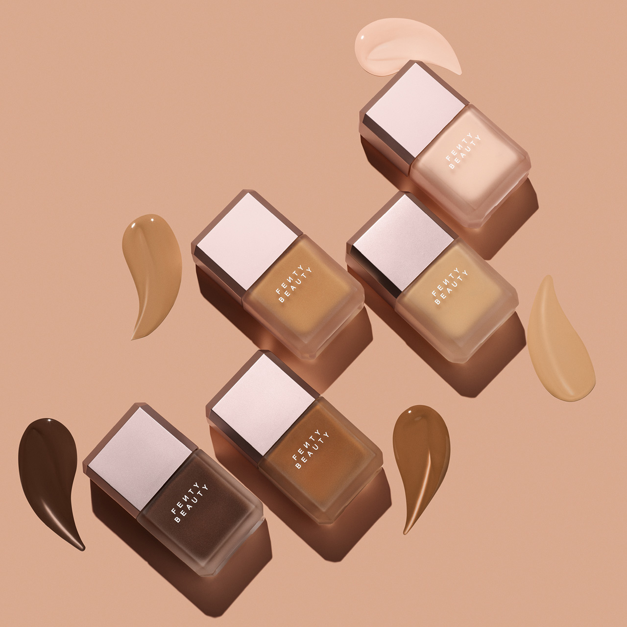 Range of Fenty Beauty foundation bottles in varying shades with liquid swatches on beige background