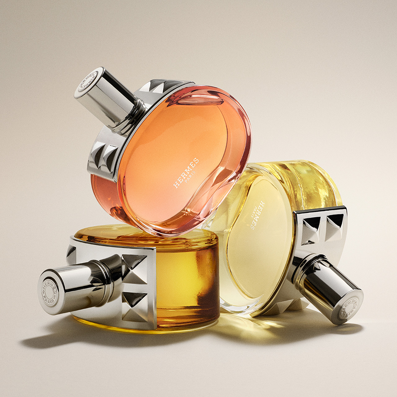 Three stylish perfume bottles with silver caps arranged artfully, featuring orange and yellow hues.