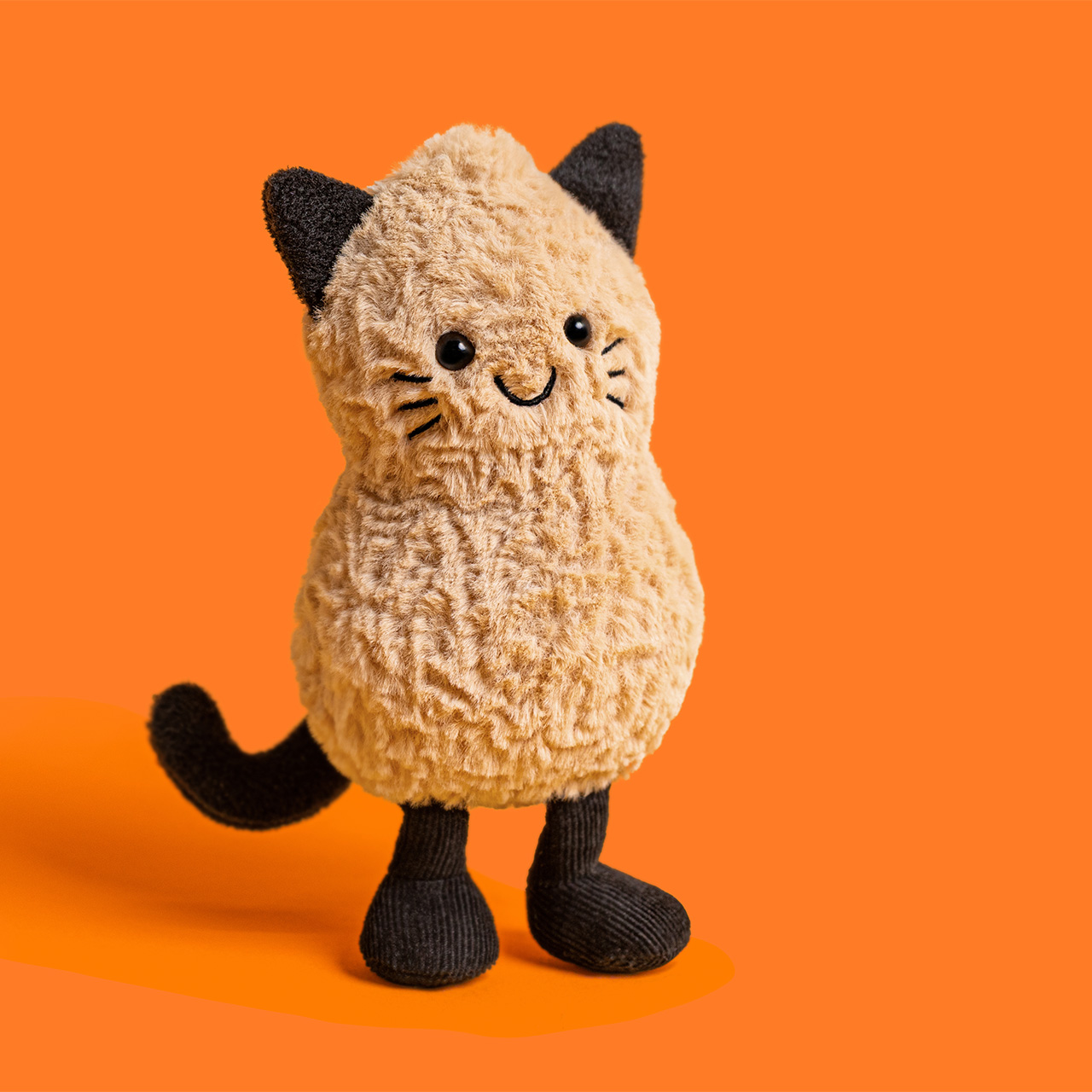 Cream and black plush cat toy with embroidered face and black ears against orange background