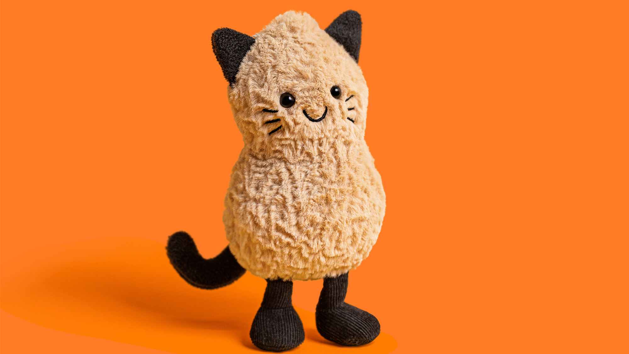 Cream and black plush cat toy with embroidered face and black ears against orange background