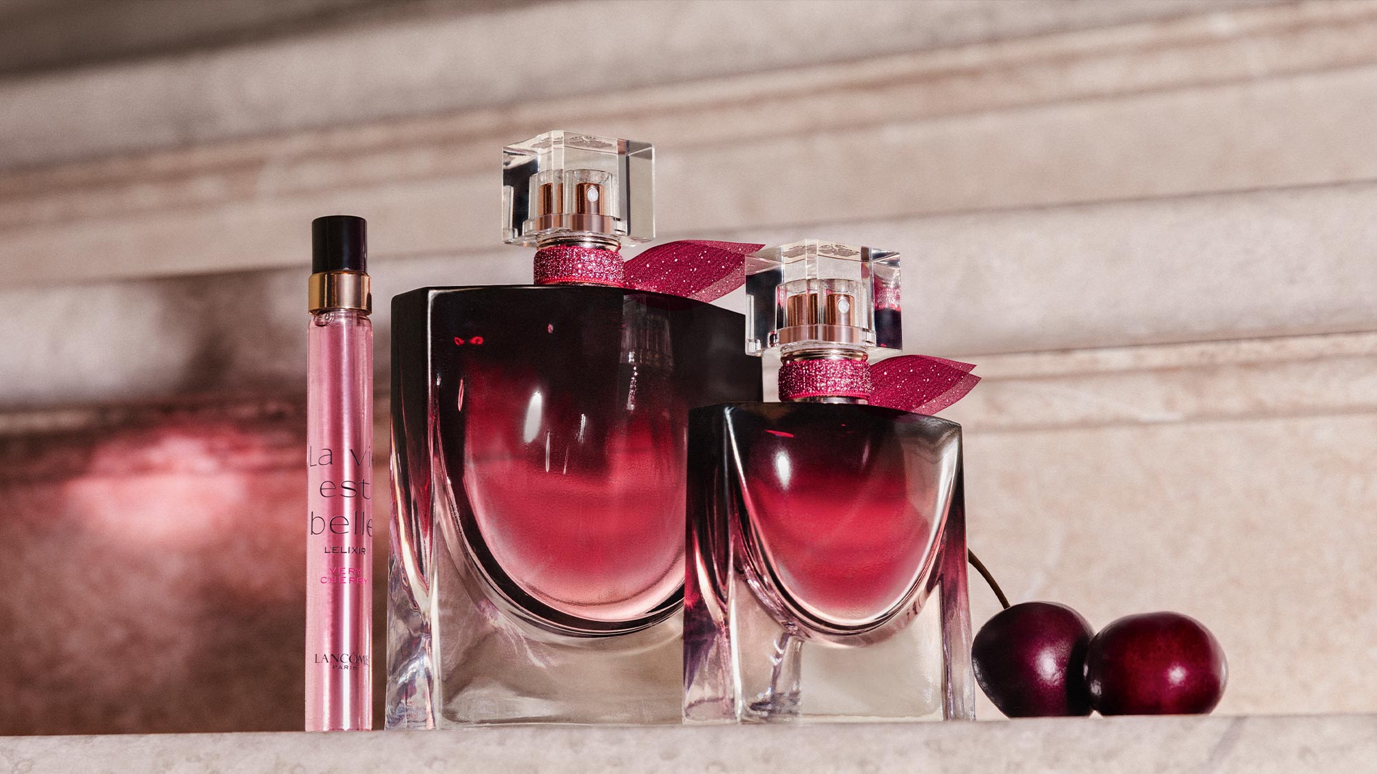 Lancôme La Vie Est Belle fragrance bottles with pink ribbon bows and burgundy baubles on neutral backdrop